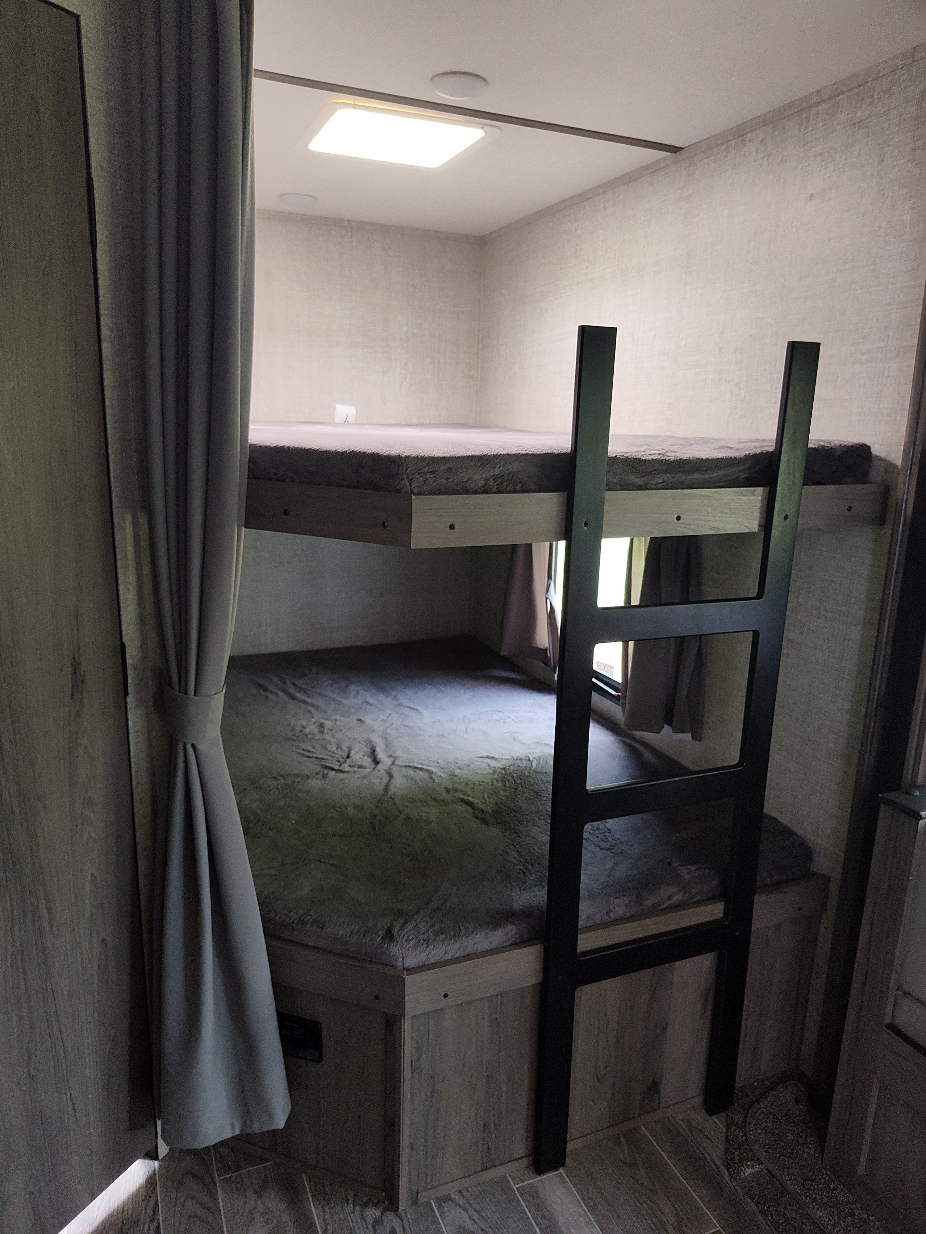 Interior of an RV rental: two gray bunk beds with ladder, soft mattresses, and a side privacy curtain.. Gulf Stream Ameri-Lite 2021