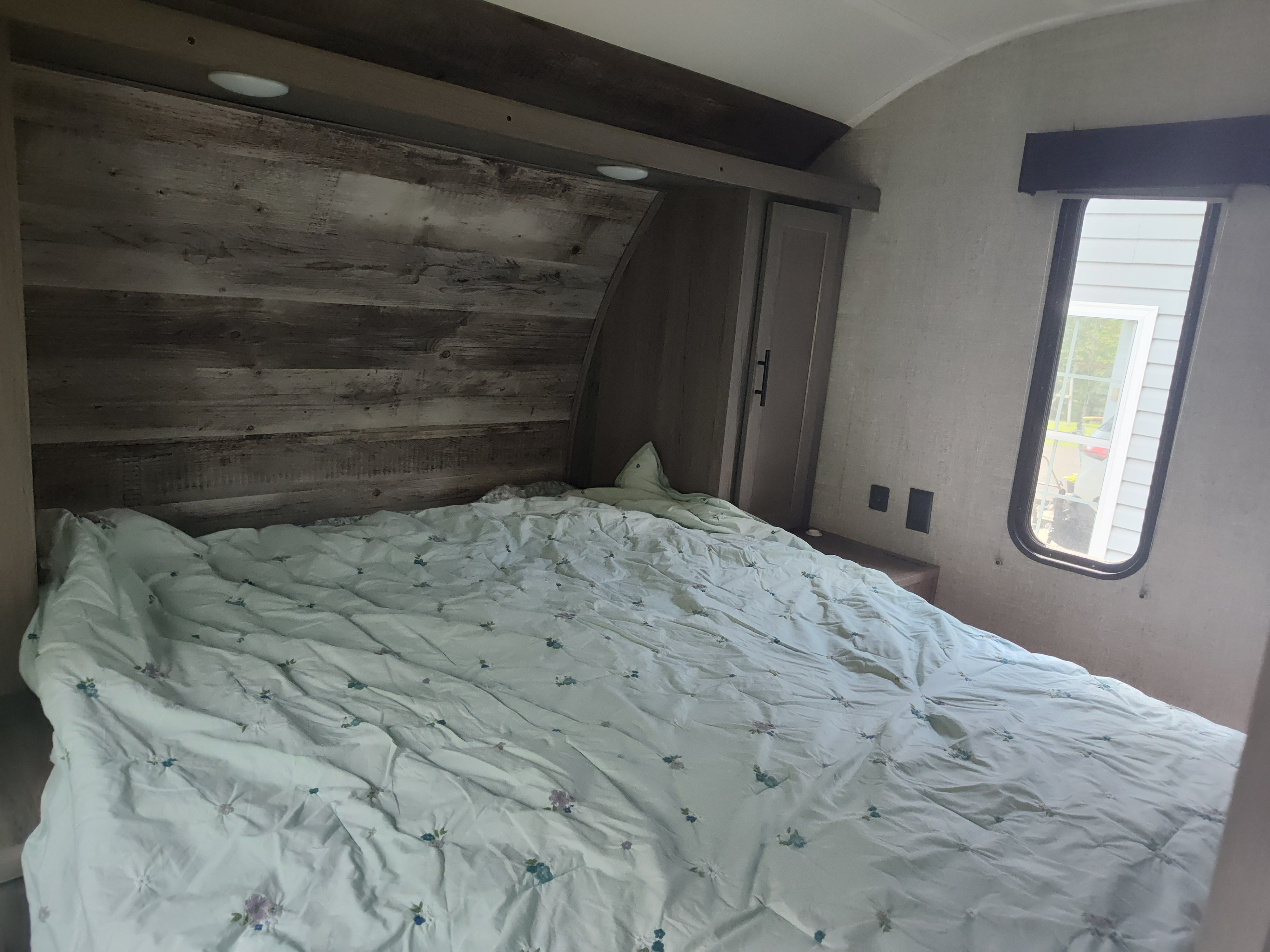 This RV rental bedroom features a comfy bed, rustic wood headboard, and natural light from the window.. Gulf Stream Ameri-Lite 2021