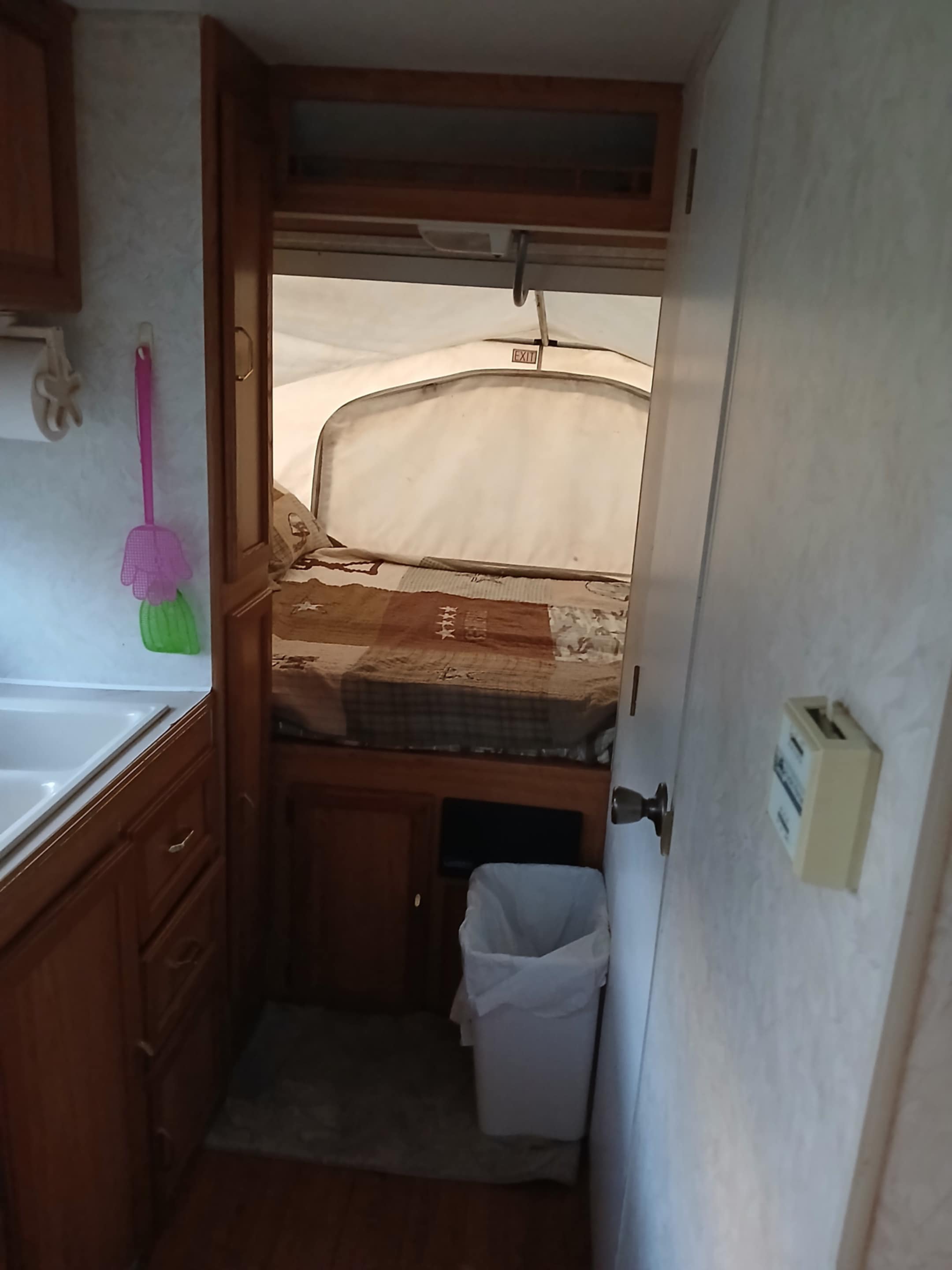 RV rental interior. View from kitchen: sink, cabinetry, and a cozy pop-up bed with an EXIT sign.. Forest River Palomino 2002