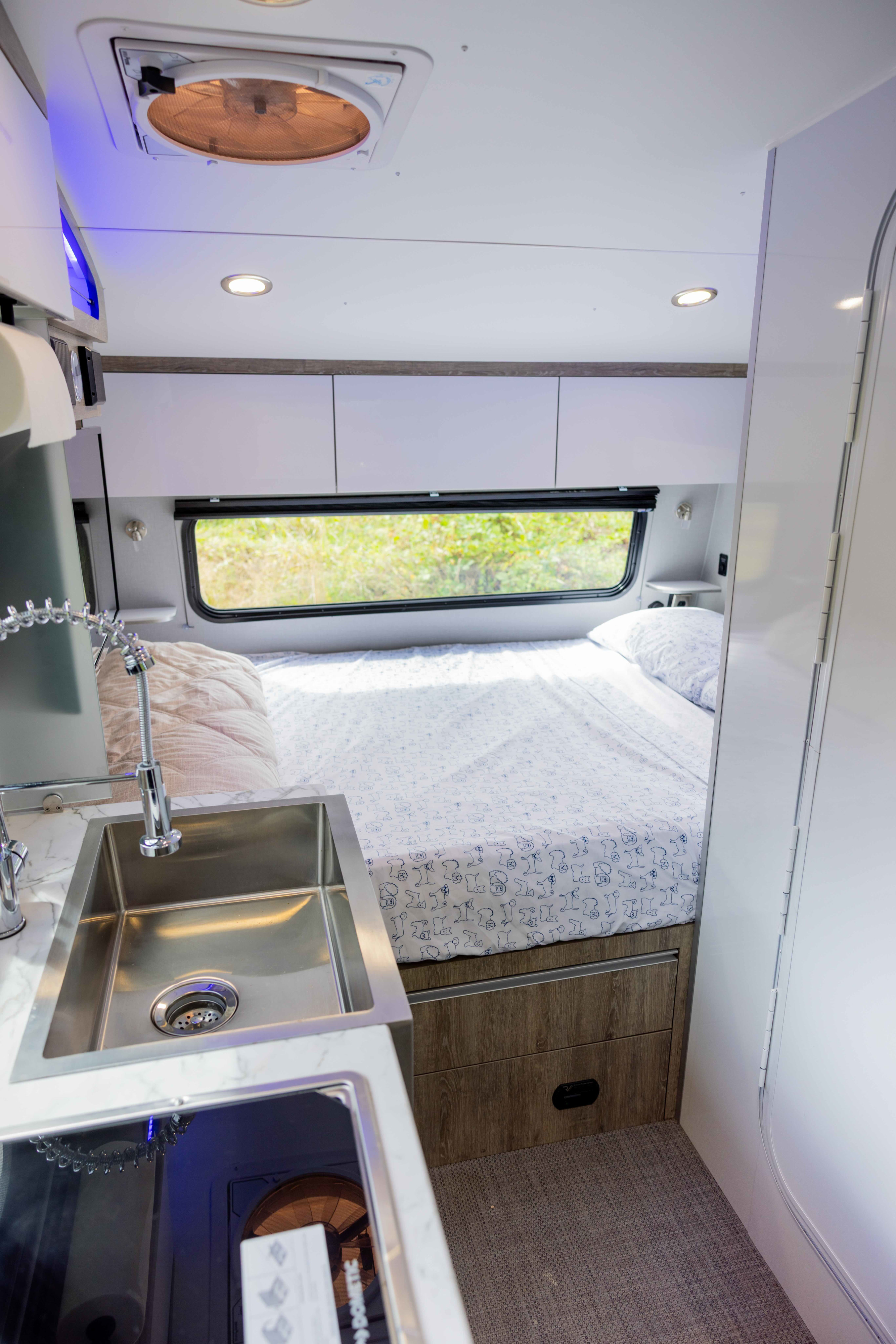 Inside this **rv rental**: a compact kitchen sink, comfy bed with patterned sheets, and overhead storage for travel.. InTech RV Sol 2022