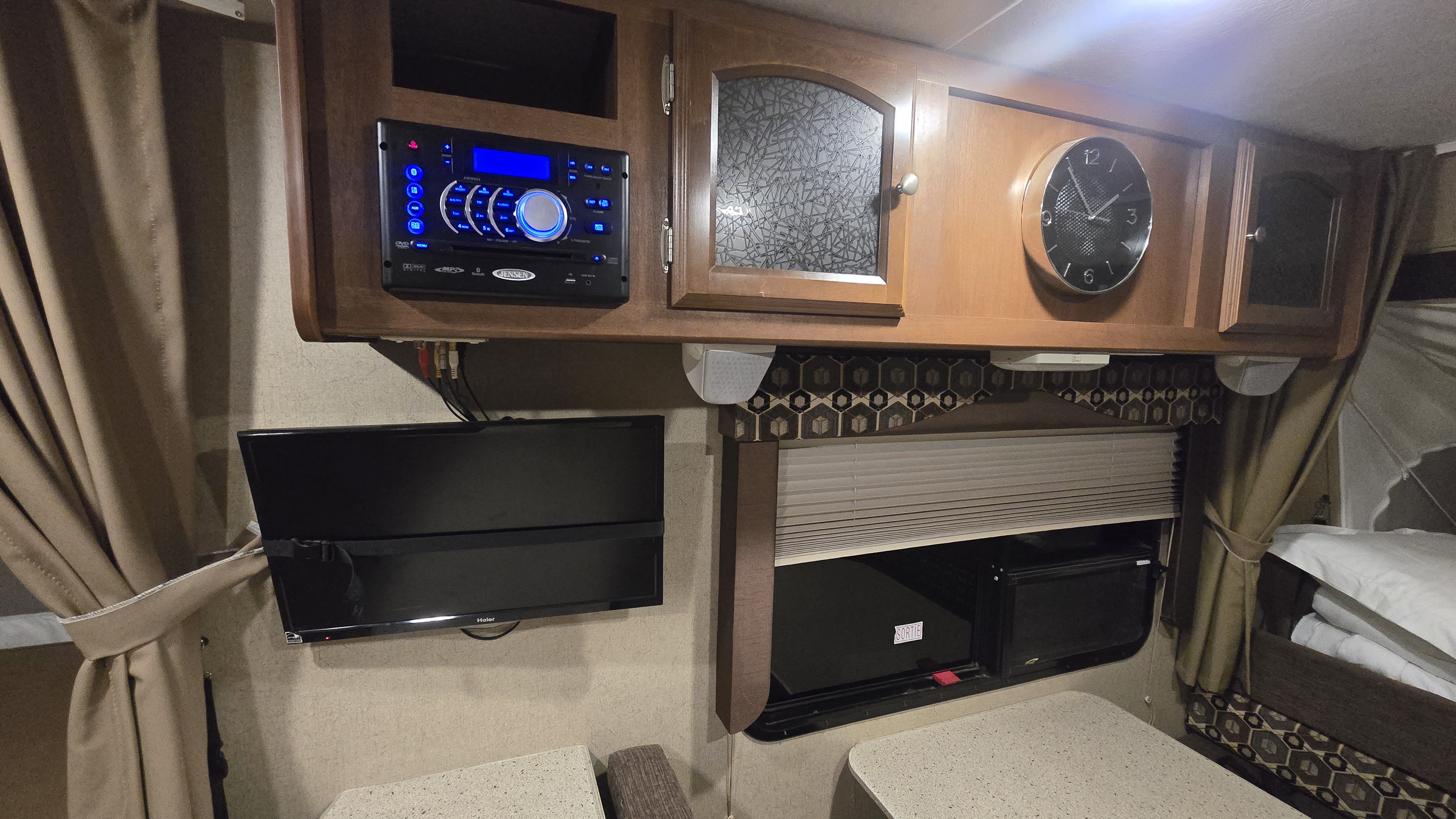 RV rental's compact entertainment and living area: stereo, TV, cabinets, clock, and window with blinds.. Coachmen Freedom Express 2015
