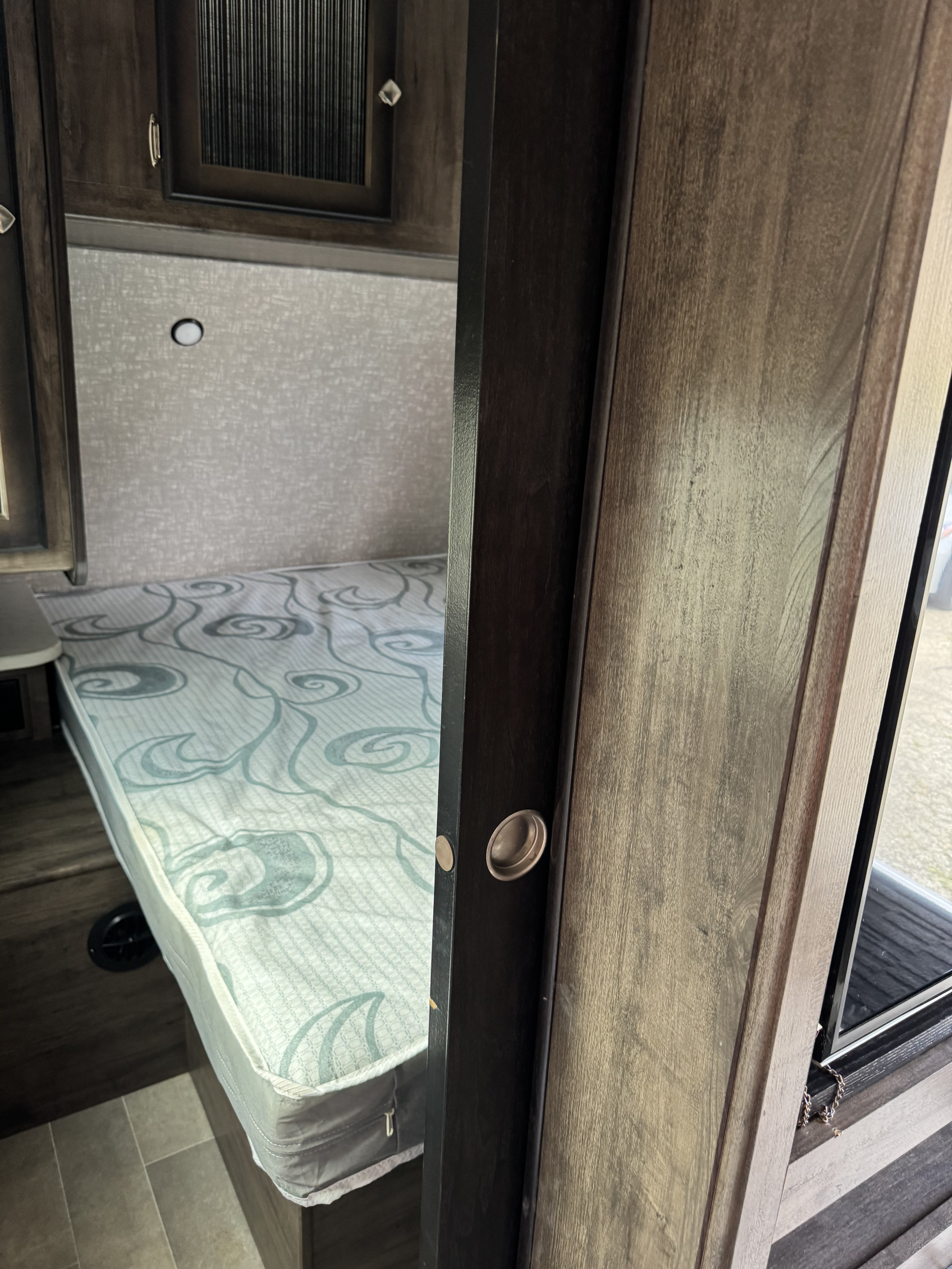 Interior of an RV bedroom showing a bed with a patterned mattress, overhead cabinetry, and a partially open sliding door. Ideal for an RV rental.. Heartland RVs Mallard 2019