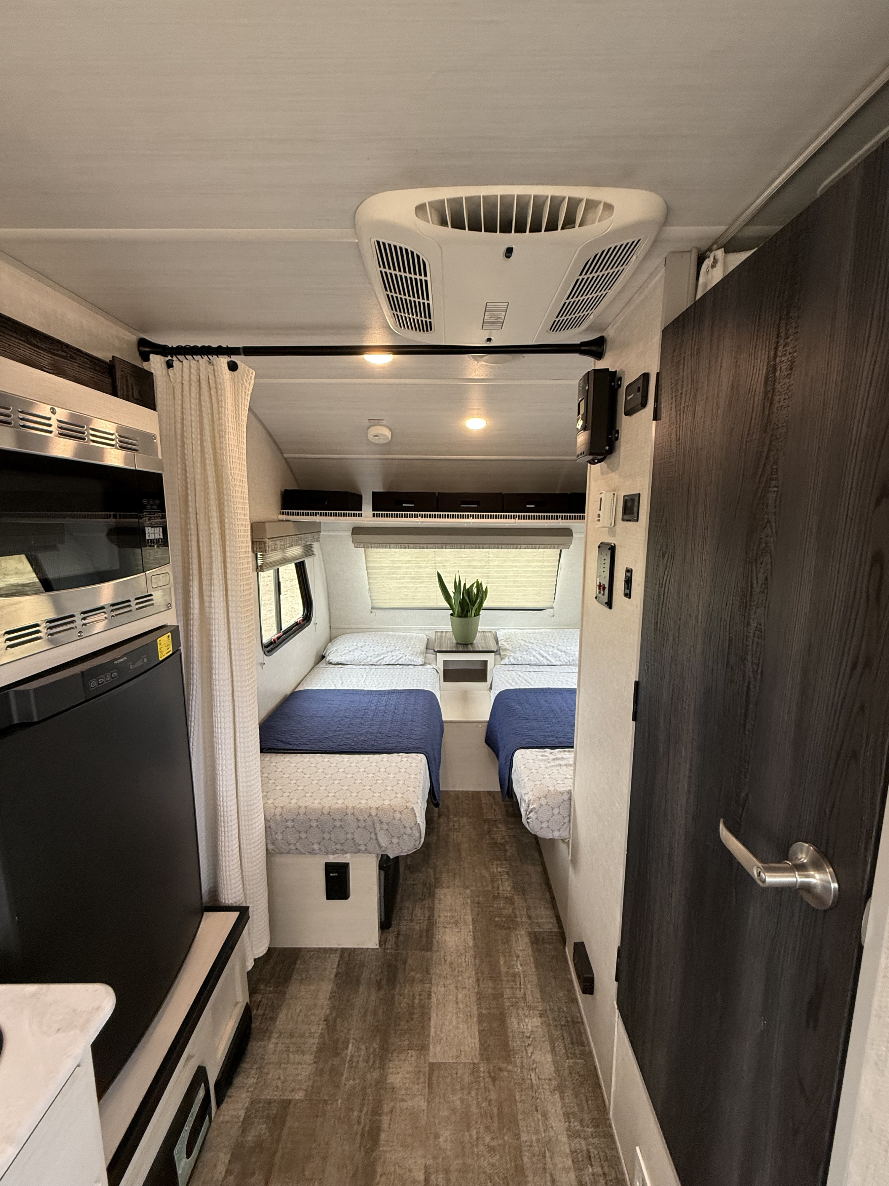 Inside a functional RV rental: twin beds, compact kitchen with microwave/fridge, and overhead AC unit for comfort.. R-Pod R-Pod Trailer 2021
