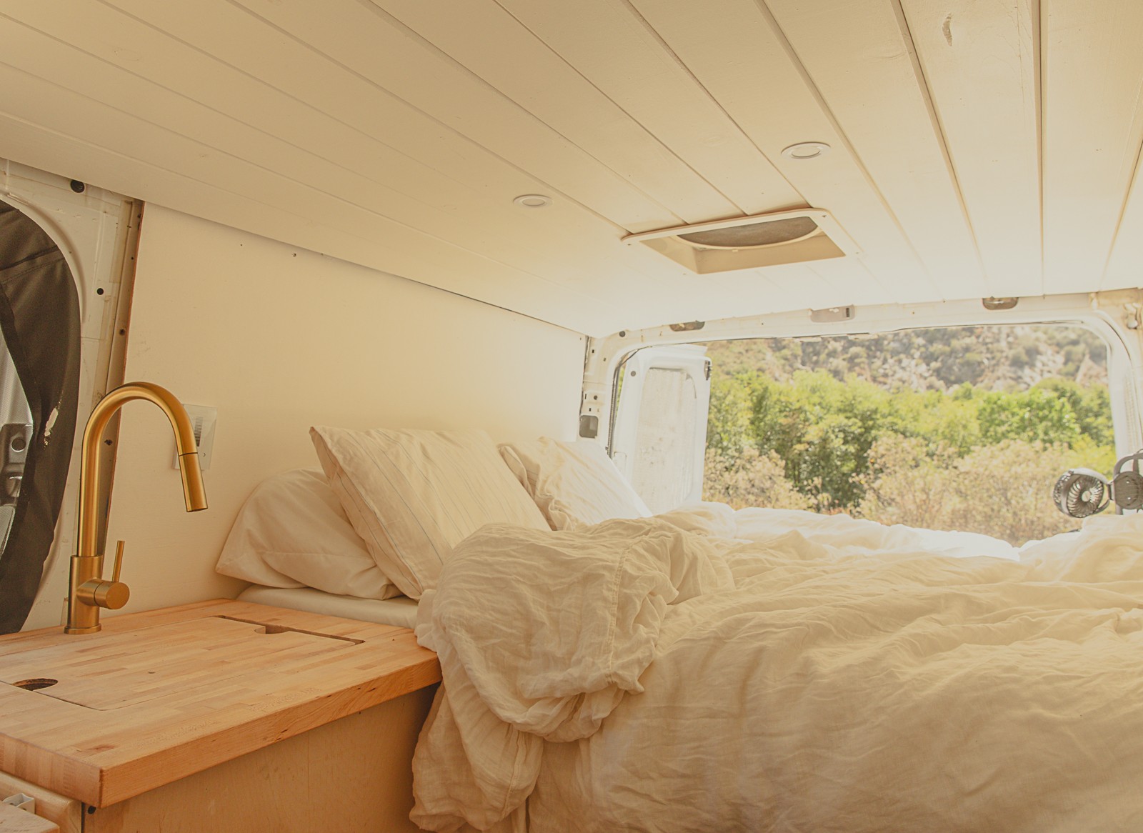 Cozy RV rental interior with bed, kitchen sink, and beautiful outdoor view, perfect for van life adventures.. Dodge Sprinter Van 2007