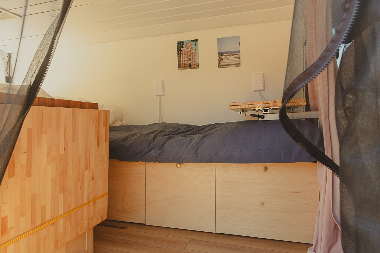 RV rental interior: cozy bed with storage, small table, wood accents, and mosquito netting for comfortable travel.. Dodge Sprinter Van 2007