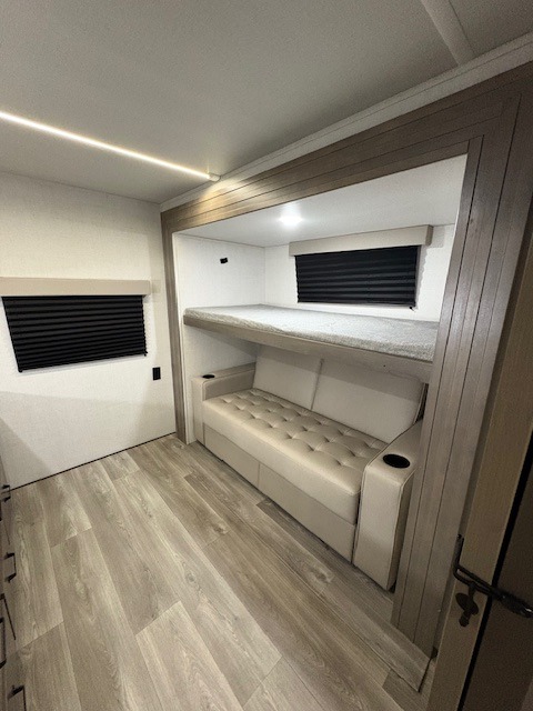 RV rental bunk room: a lower sofa bed with cupholders & an upper bunk. Bright, modern interior with wood-look floor.. Grand Design Transcend Xplor 2024
