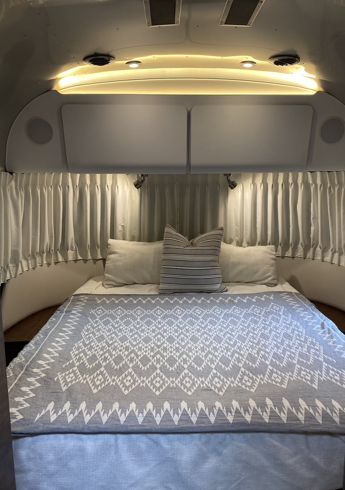 Cozy RV rental bedroom featuring a patterned bed, soft lighting, and window curtains, ideal for comfortable travel.. Airstream Globetrotter 2019