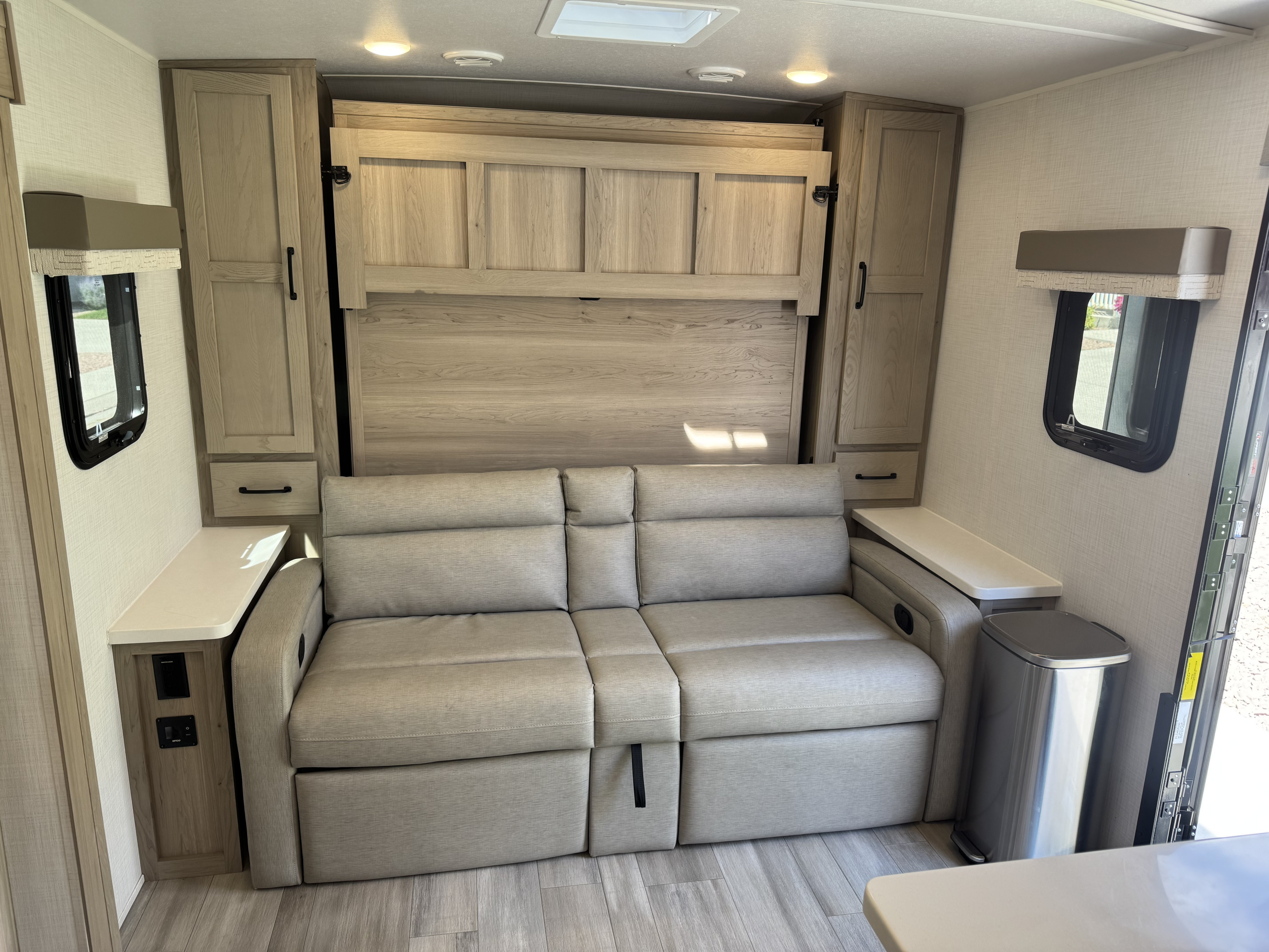 Interior of an RV rental featuring a light grey sofa that converts into a bed, flanked by wooden cabinets and side tables.. Forest River Flagstaff Micro Lite 2024