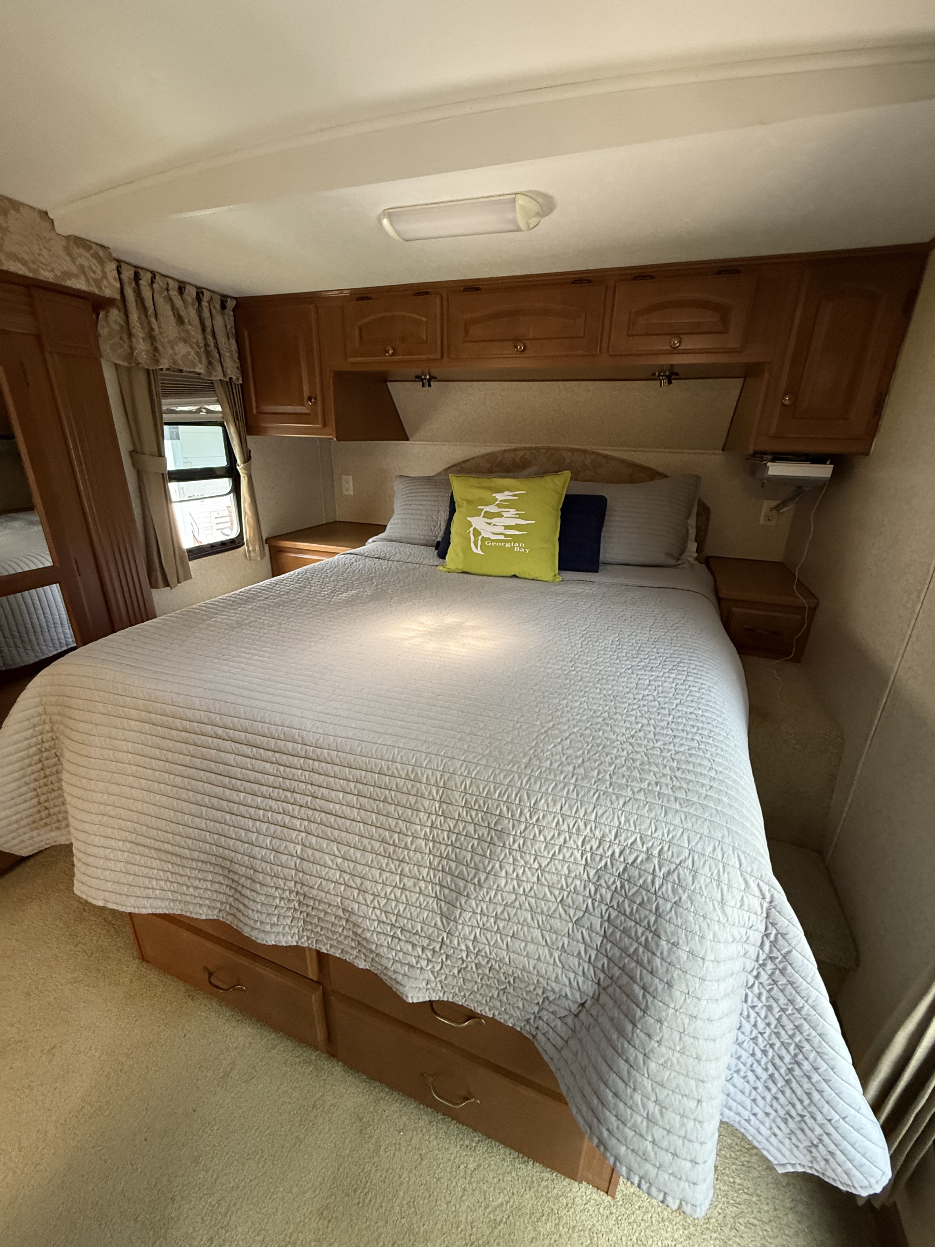 Spacious RV rental bedroom with a large bed, light grey comforter, overhead cabinets, and bedside storage for a comfortable trip.. Glendale Titanium 2008