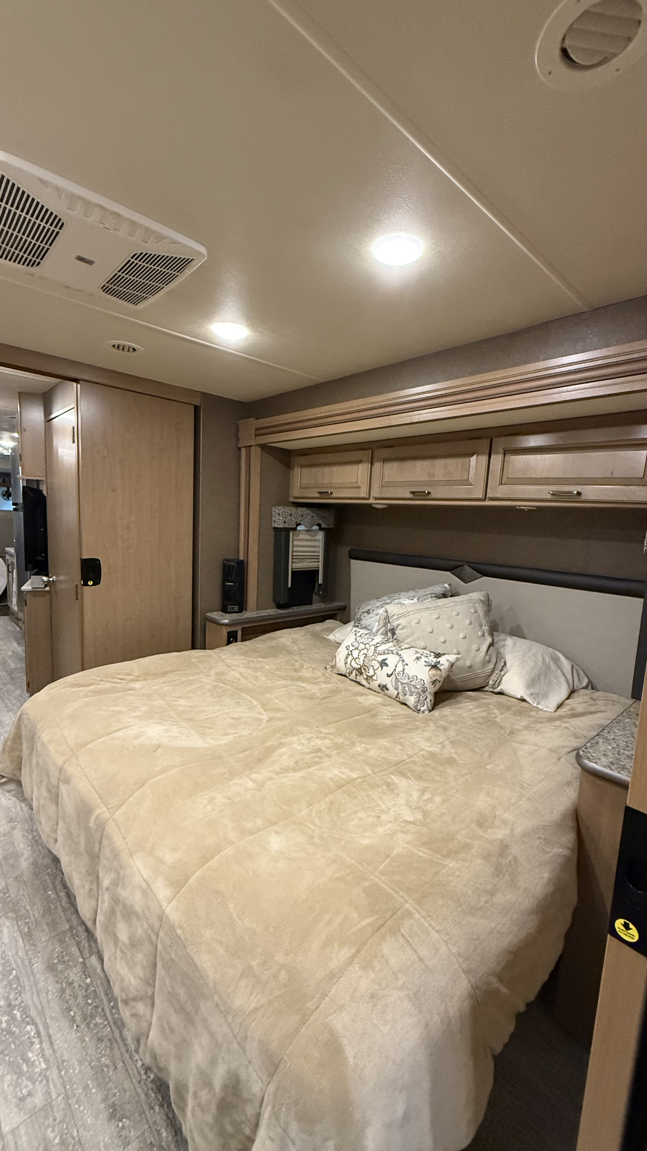 Comfortable RV rental bedroom with a large bed, plush bedding, overhead cabinets, and ceiling AC unit. Perfect for travel.. Thor Hurricane 2019