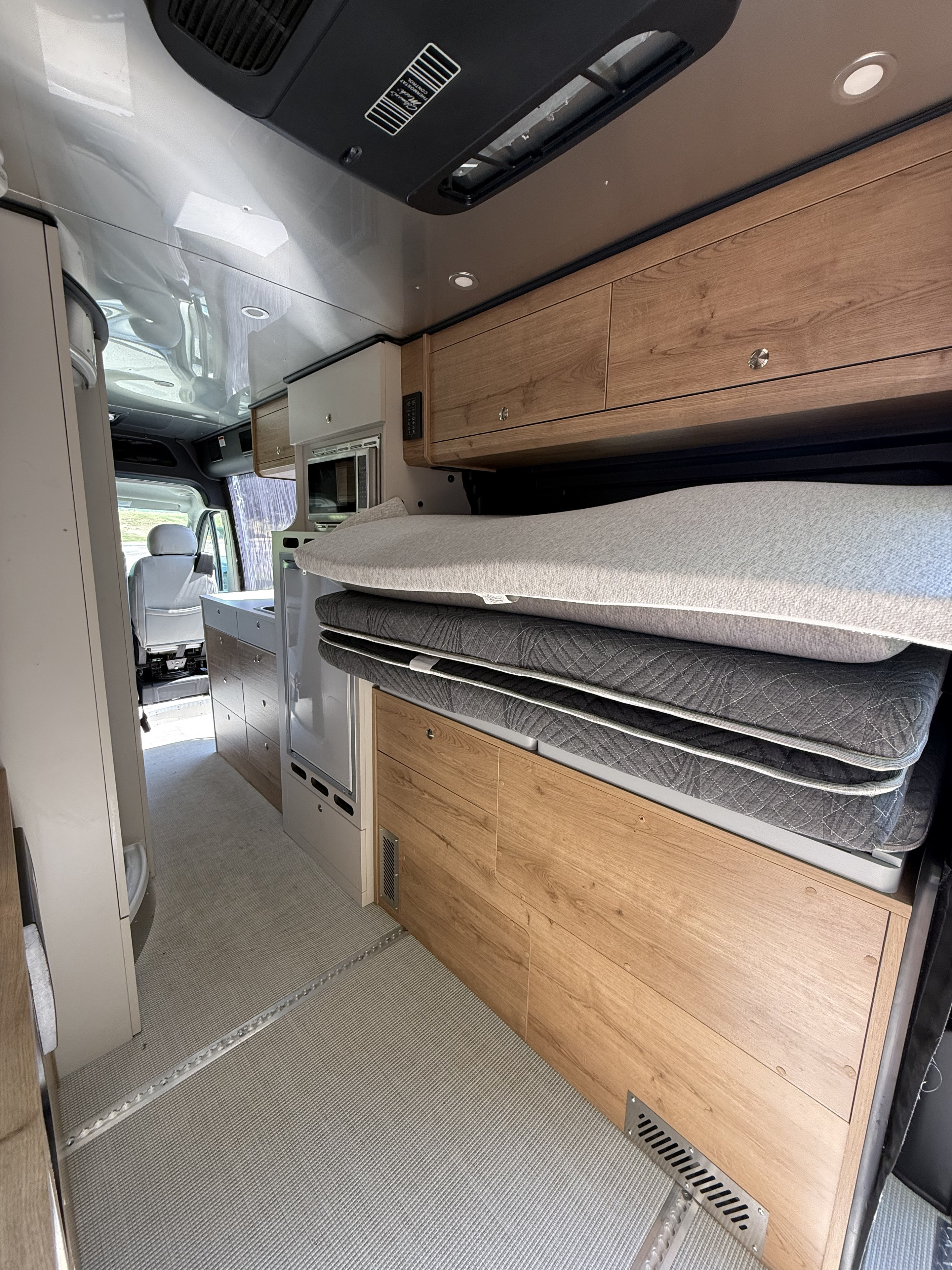 Inside an RV rental camper van: light wood interior, modern kitchen, and a cleverly stowed bed for comfortable travel.. Airstream Airstream Class B 2023