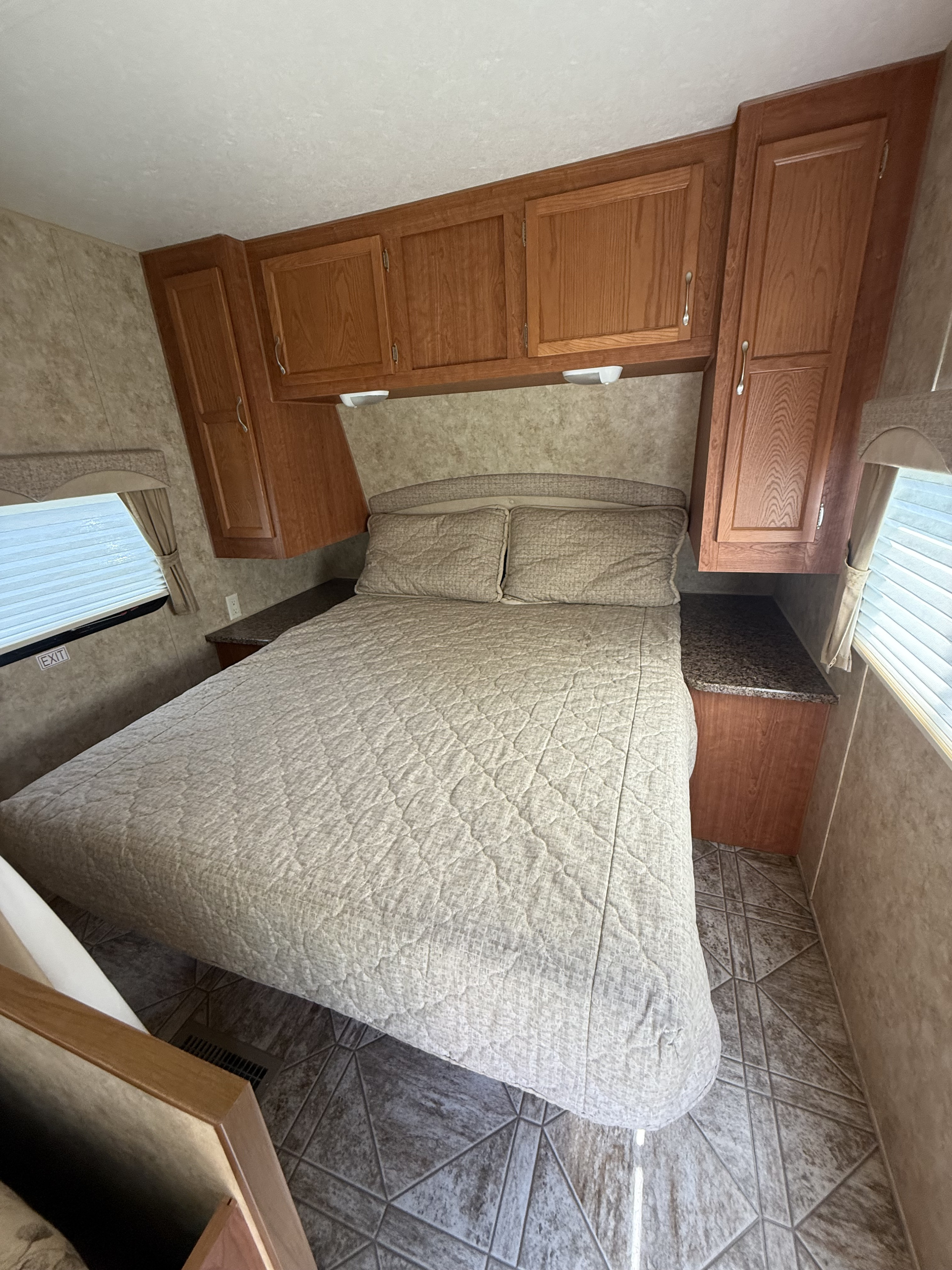 Comfortable RV rental bedroom featuring a cozy bed, overhead cabinets, and windows with blinds.. Starcraft Autumn Ridge 2010