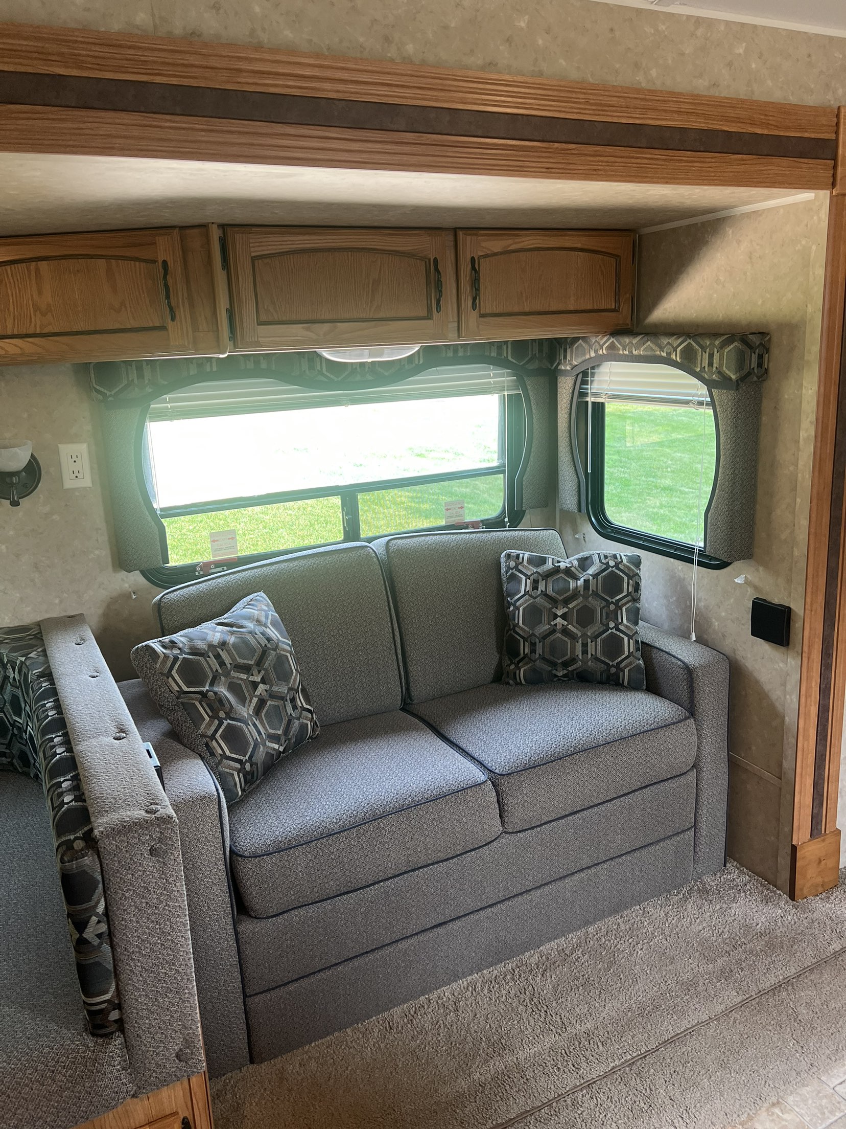 RV rental living area: gray sofa with accent pillows, overhead cabinets, and bright windows offering outdoor views.. Forest River Palomino Puma 2010