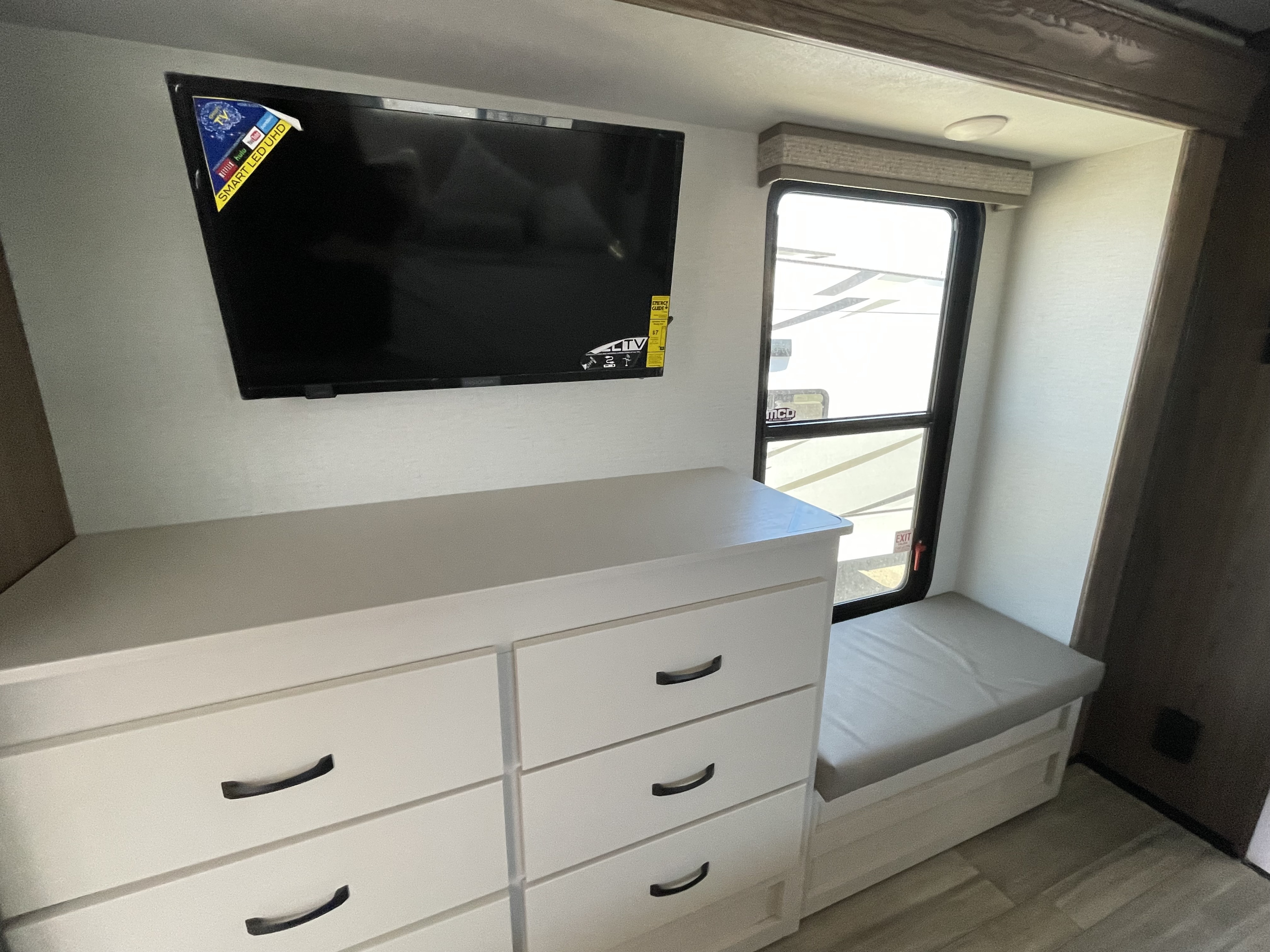 Inside an RV rental: a wall-mounted smart TV, white dresser with drawers, a window, and a bench seat.. Alliance RV Paradigm 2023