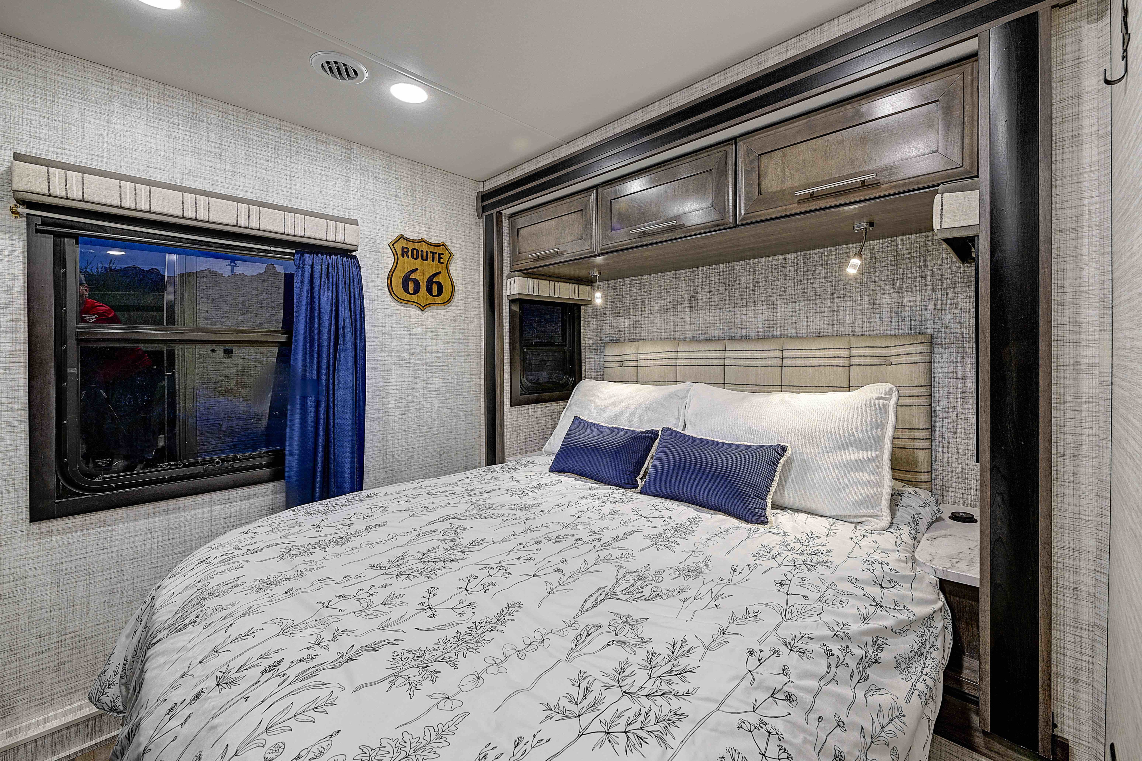 RV rental bedroom with stylish white and blue bedding, overhead cabinets, and a "Route 66" sign for cozy travel.. Entegra Esteem 2025