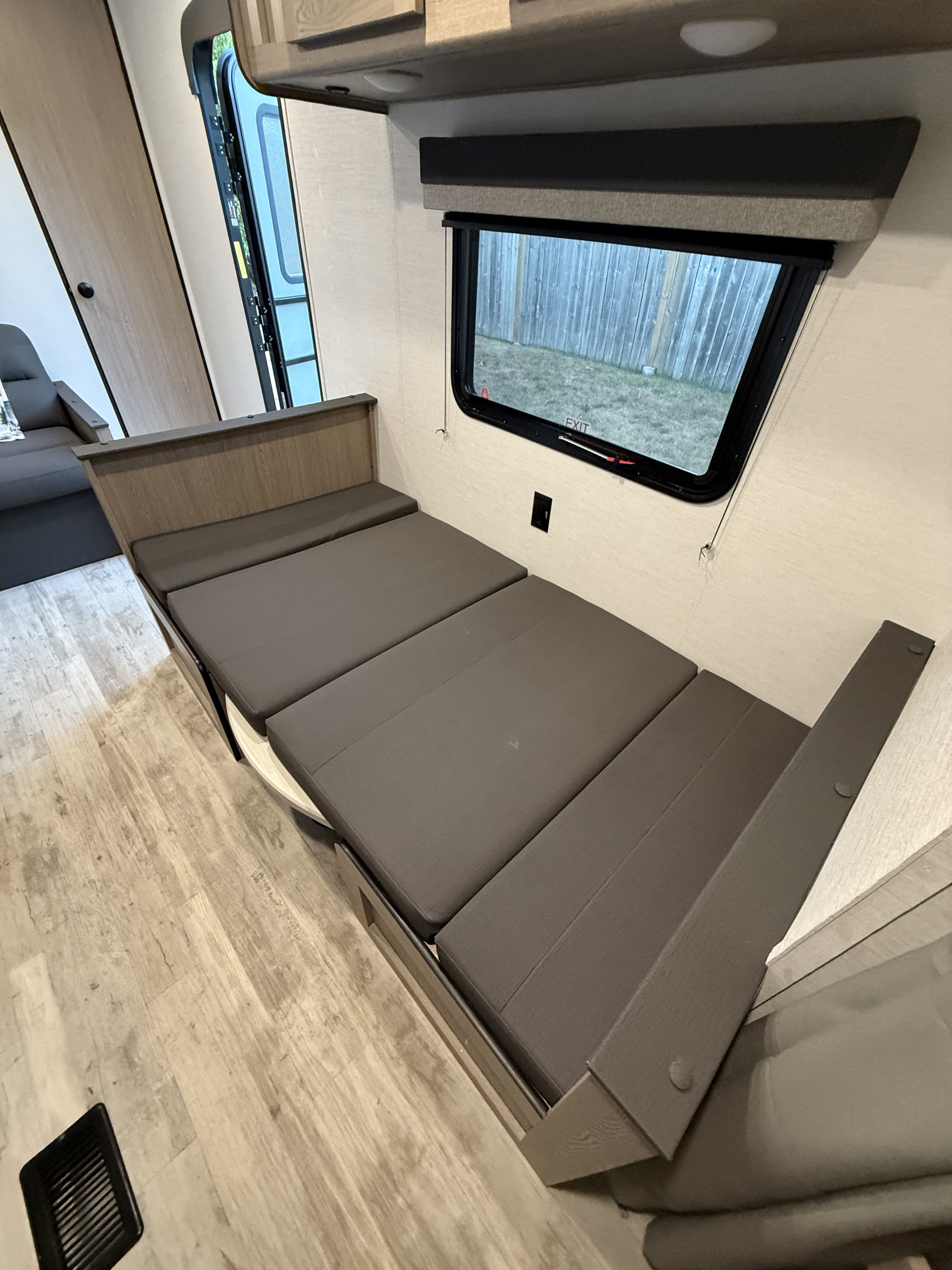 Inside this modern **rv rental**, a versatile dark grey dinette converts to a bed, with light wood flooring and a large window.. Gulf Stream Grand river 2026