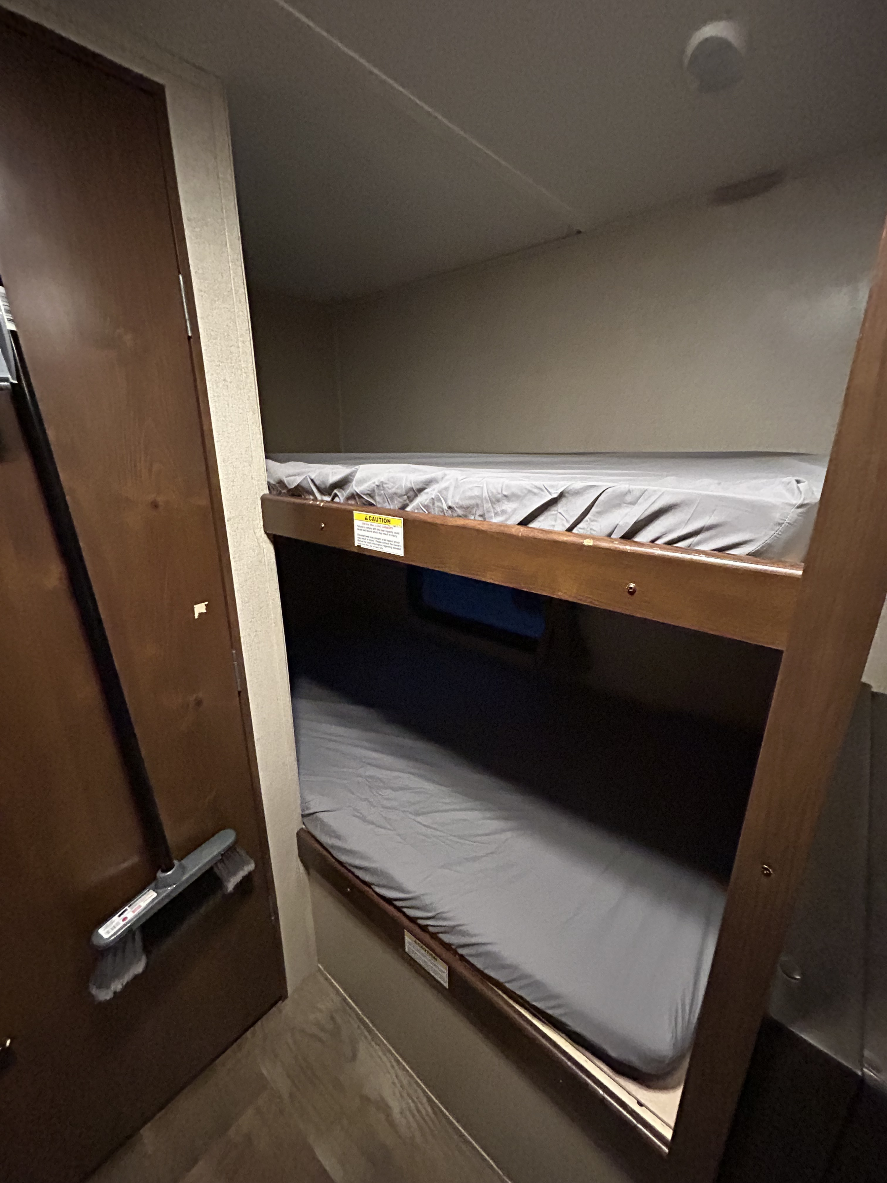 RV rental bunk bed sleeping area with two beds, grey sheets, and a broom by the adjacent door.. Crossroads RV Z-1 Lite 2017
