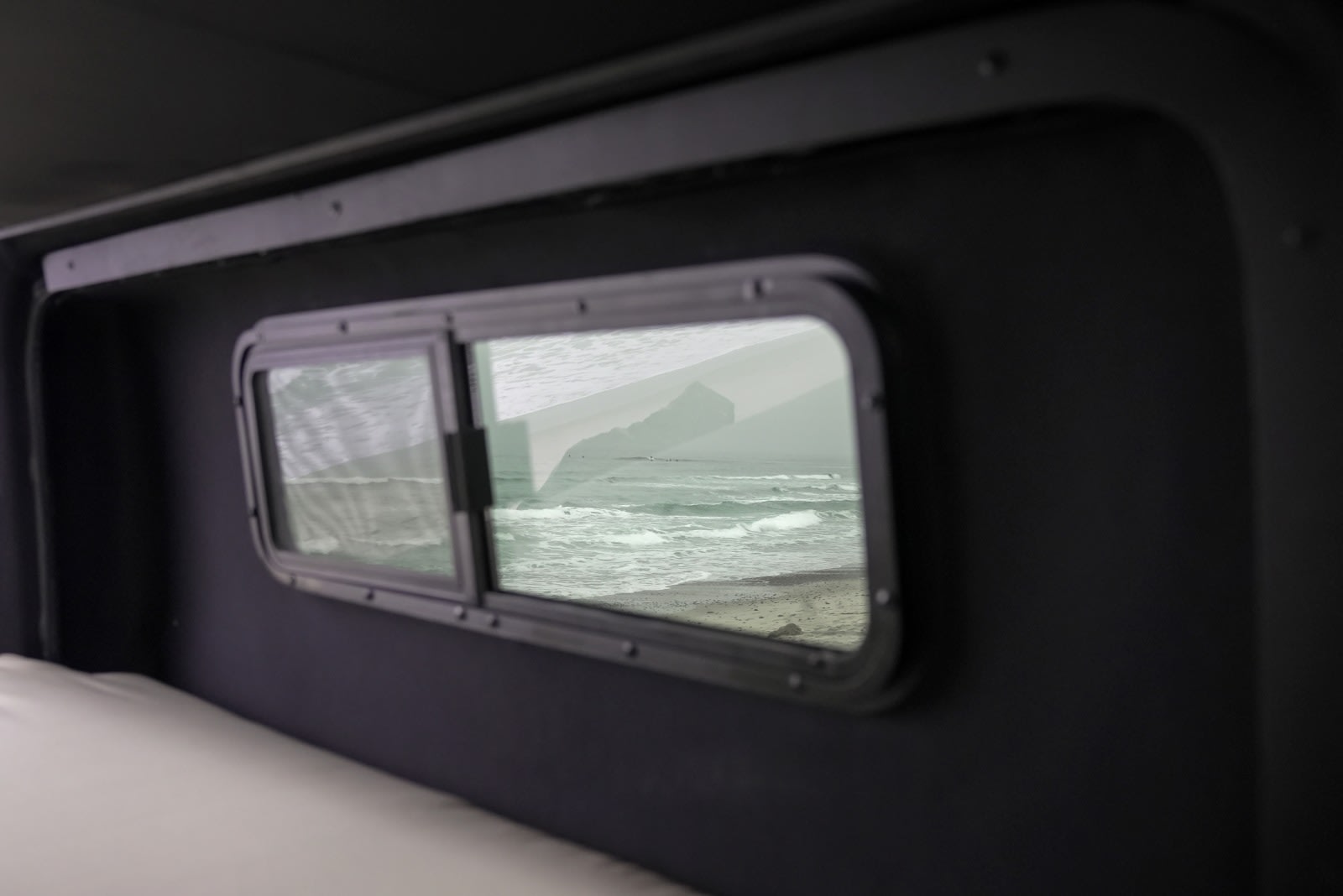 Cozy RV rental interior, window offers ocean beach view with waves & distant bluff. Ideal for travel.. Mercedes-Benz Sprinter 2021