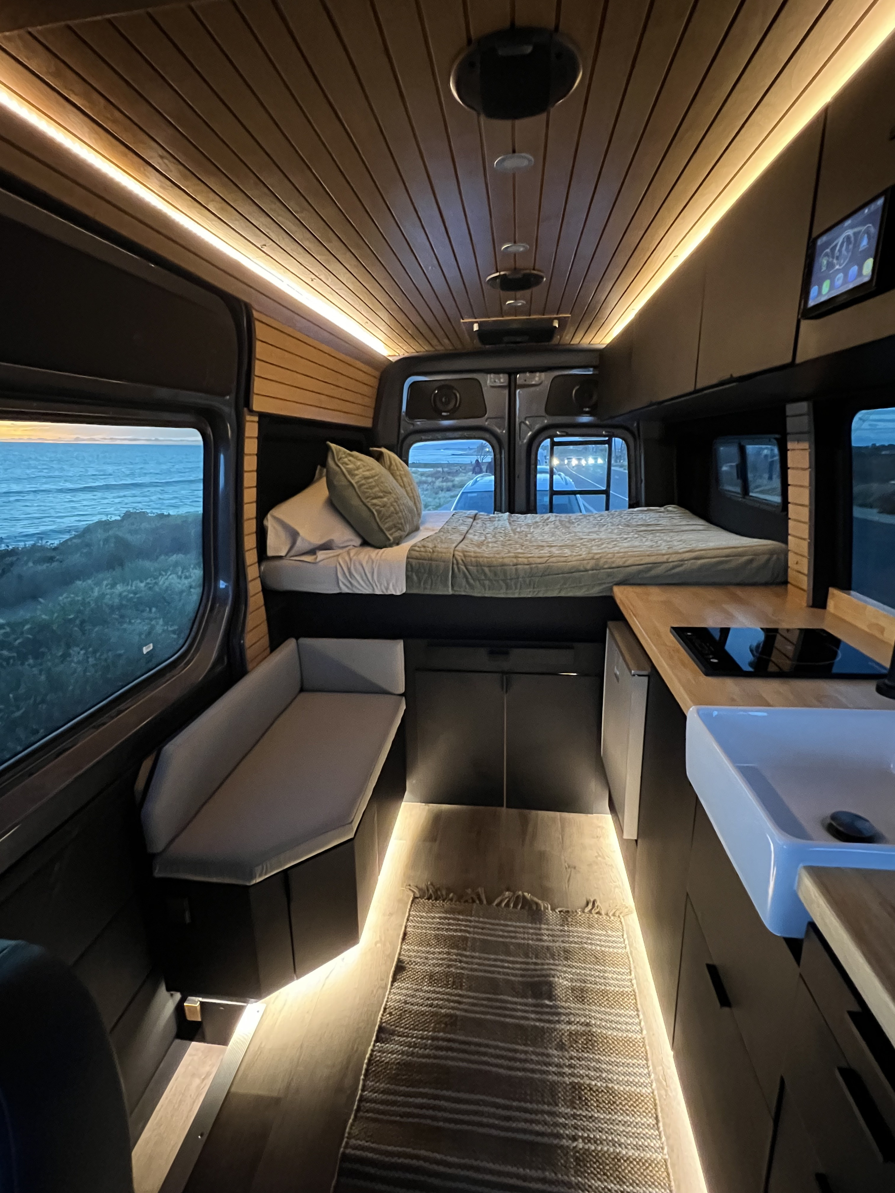 Cozy RV rental interior with a comfortable bed, kitchen, seating, and scenic ocean views, ideal for a road trip.. Mercedes-Benz Sprinter 2021