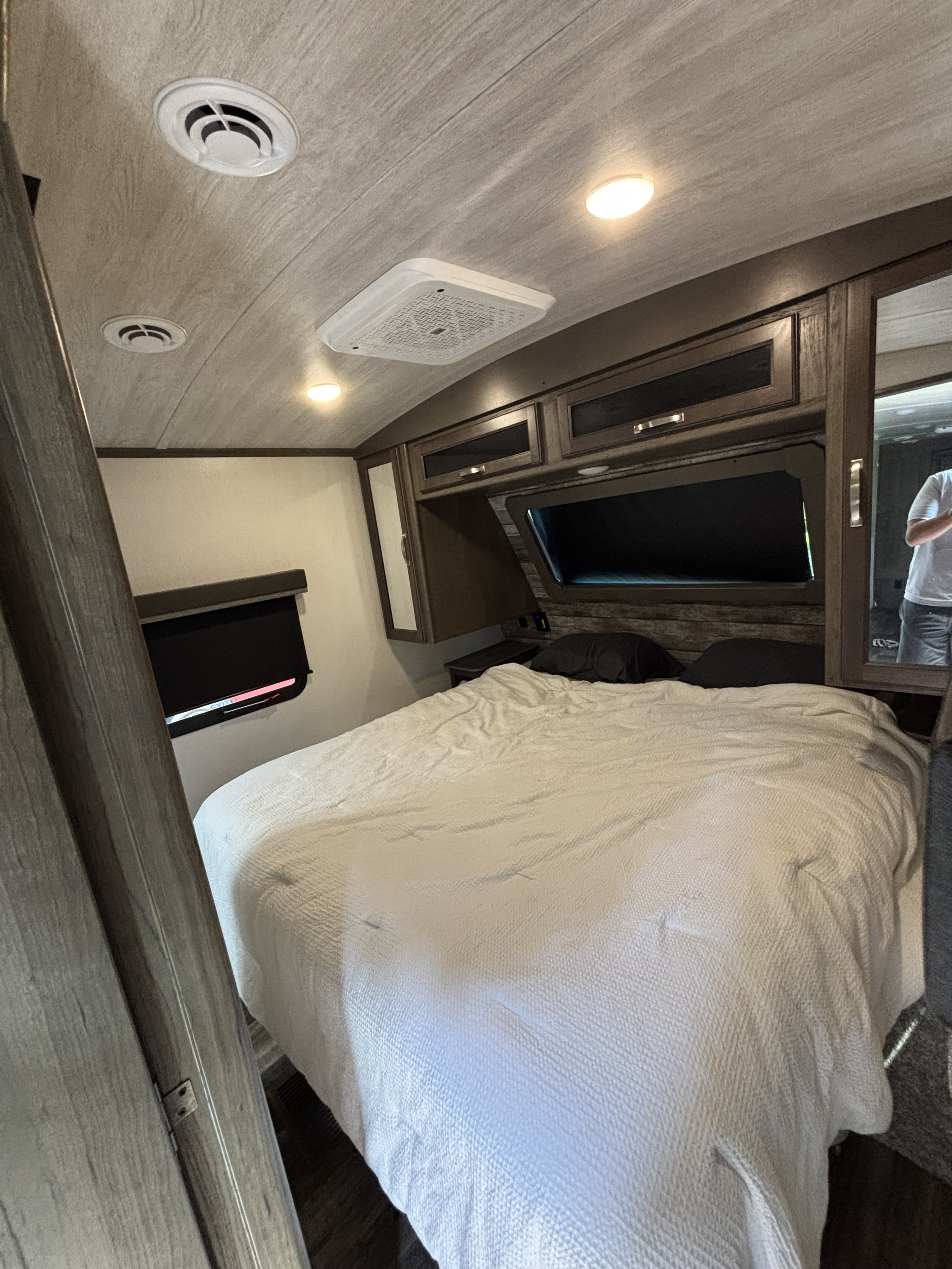 Bright RV rental bedroom with a large white bed, dark wood cabinets, and ceiling vents.. Keystone RV Cougar 2023