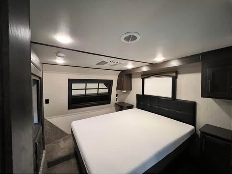 Spacious RV rental bedroom with a large bed, dark headboard, and window. Perfect for comfortable travel.. Keystone Raptor 2018