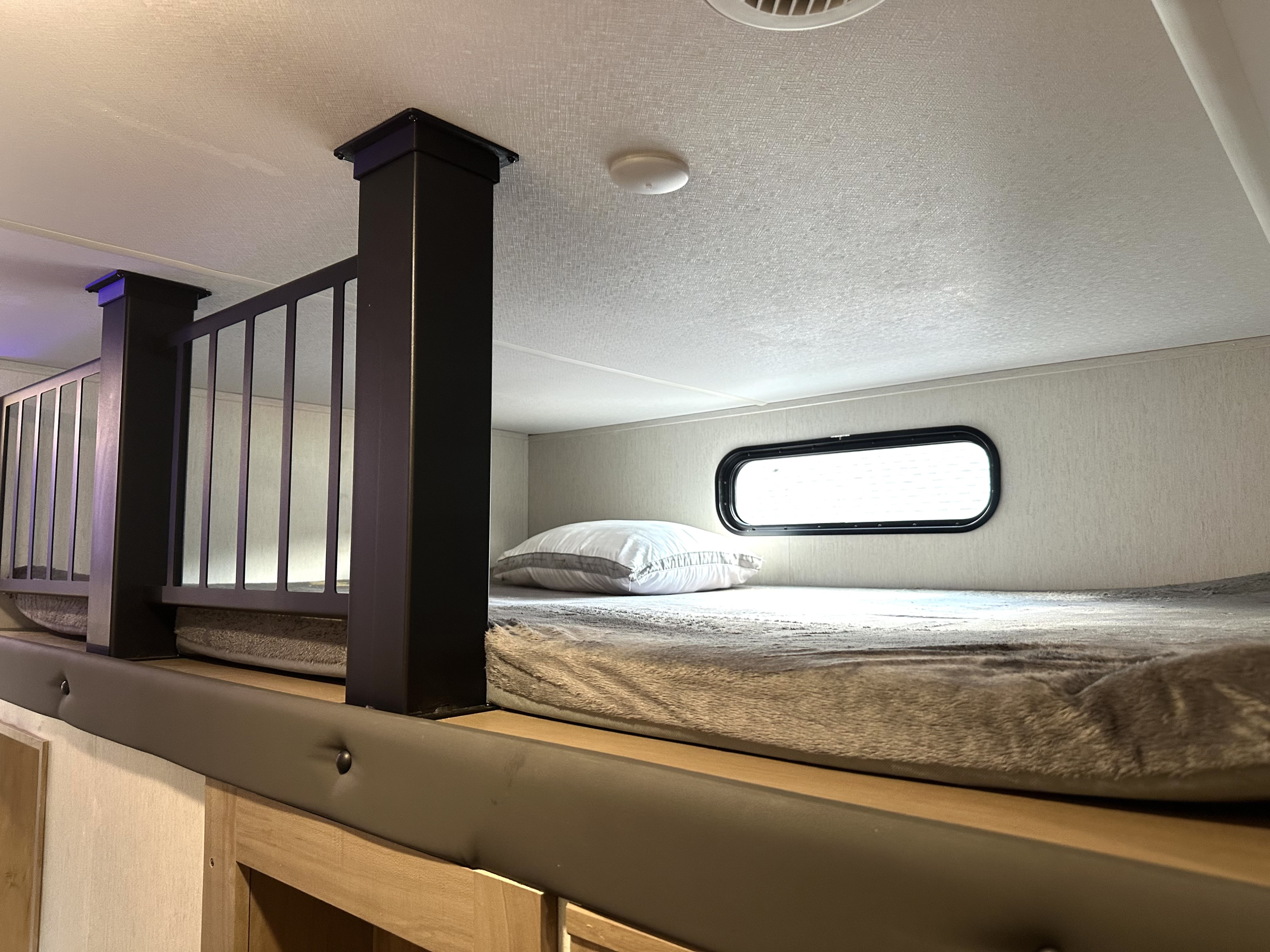 Inside an RV rental: a modern bunk bed setup with safety railing, plush mattress, and window.. Forest River Cherokee Arctic Wolf 2023