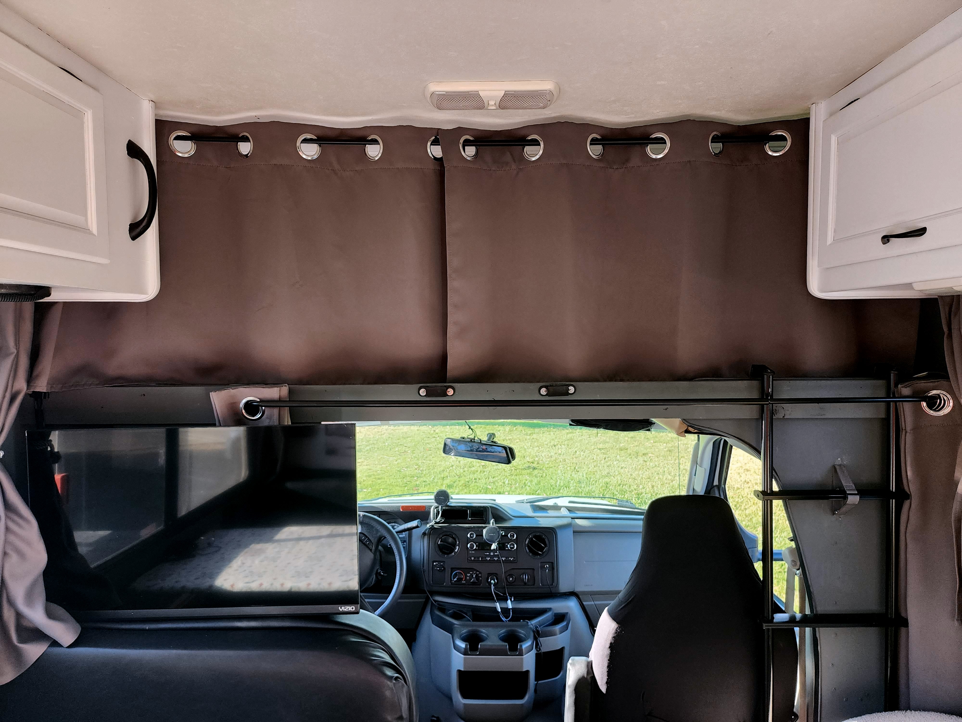 Inside an RV rental: brown privacy curtains separate the cozy living area with TV from the front cab.. Thor Majestic 2017