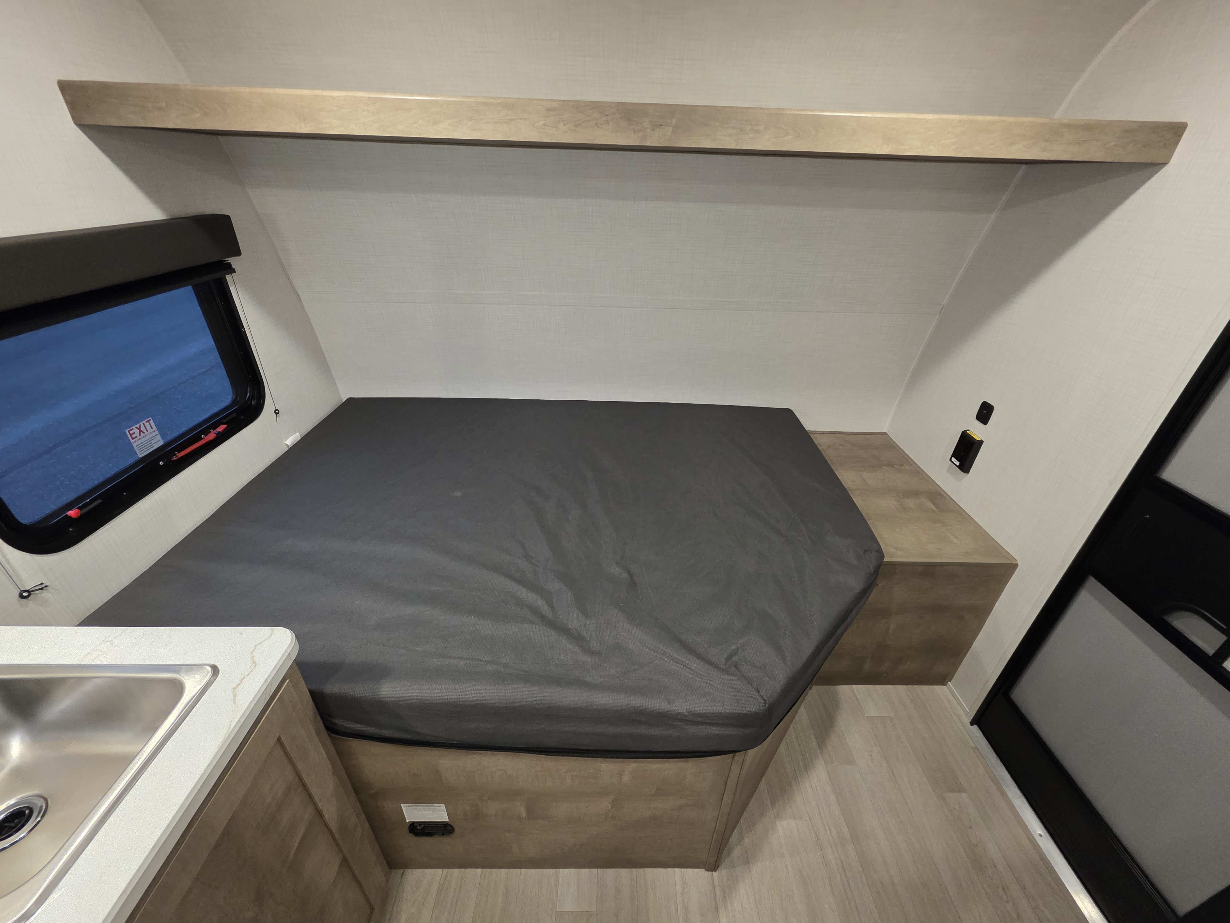 RV rental interior: A compact sleeping area with a grey bed, emergency exit window, and small sink. Ideal for road trips.. Keystone Springdale 2026