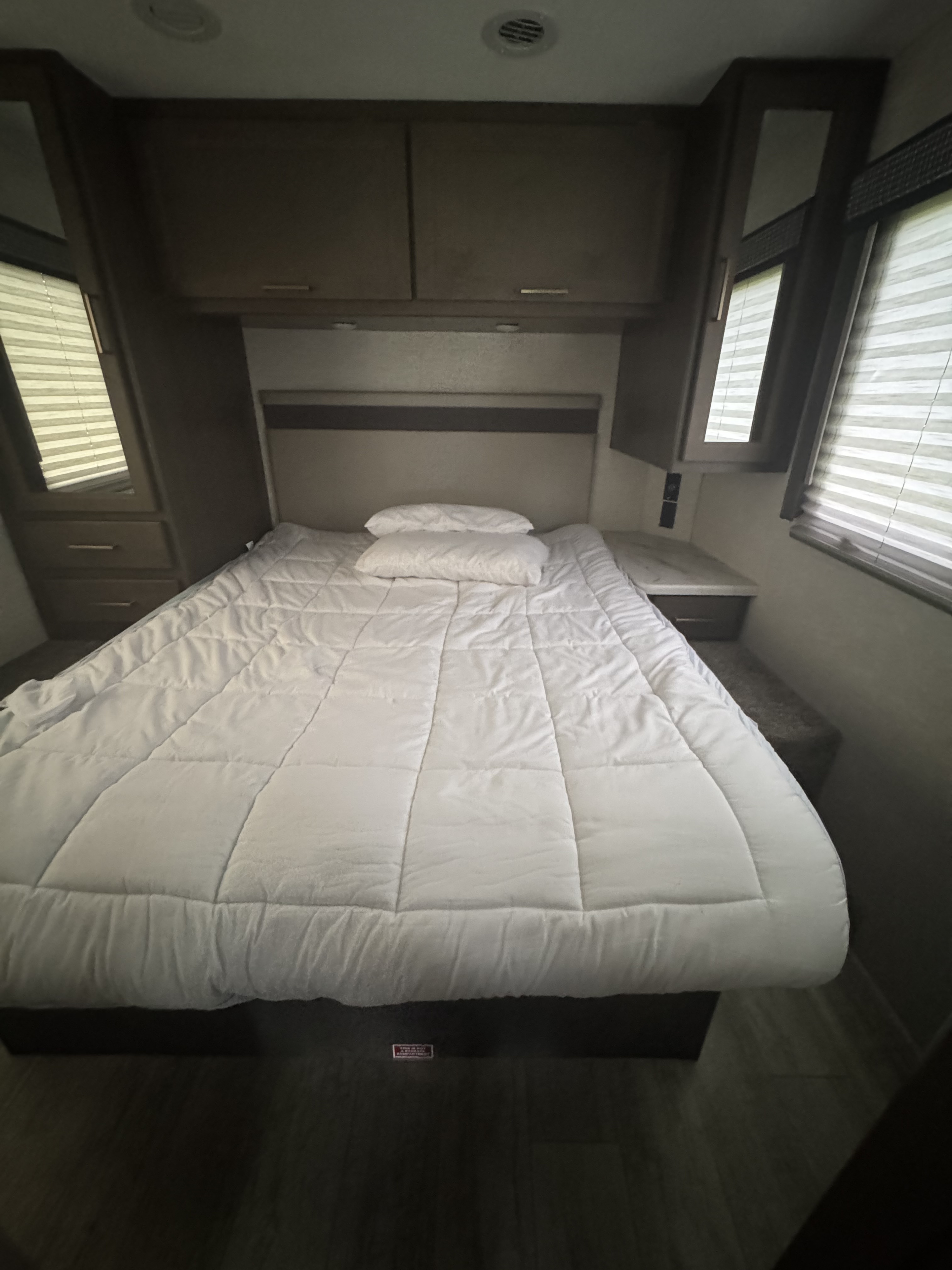 This RV rental shows a compact bedroom featuring a bed with a white comforter, overhead storage, and windows with blinds.. Thor Chateau 2024