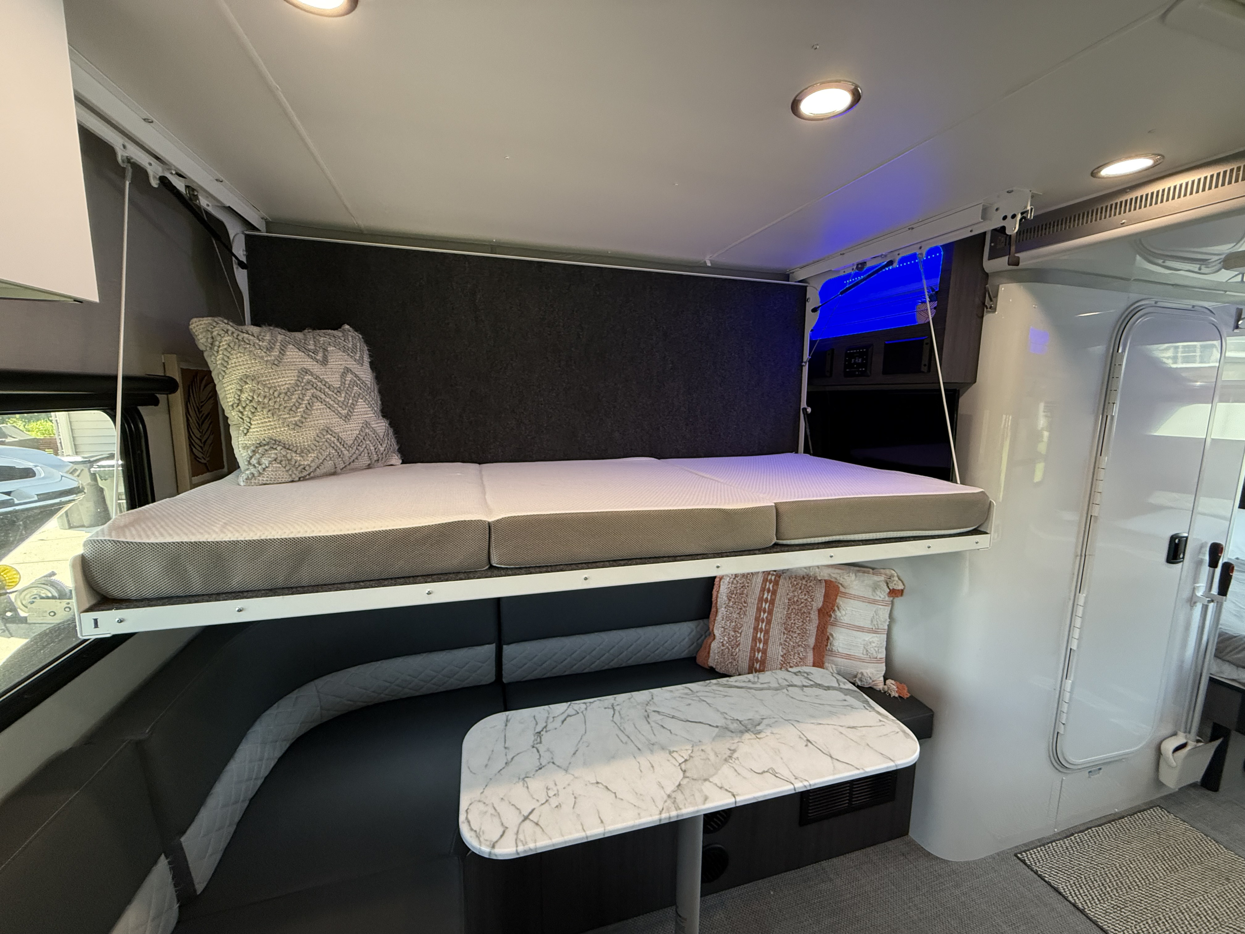 This RV rental interior features a cozy upper bunk bed, lower dinette with a modern table, and ambient lighting.. InTech RV O-V-R 2023