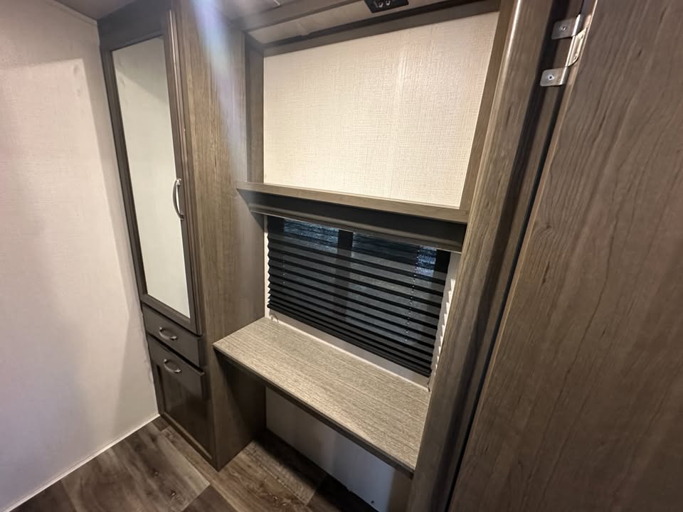 This RV rental interior features a mirrored closet, lower drawers, a window with blinds, and a small built-in desk.. Keystone RV Cougar 2021