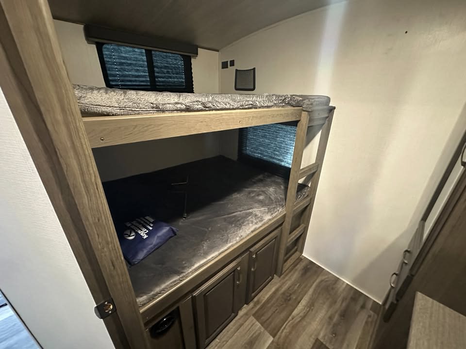 Functional bunk beds in an RV rental, showing stacked sleeping areas with a window & storage for comfortable travel.. Keystone RV Cougar 2021