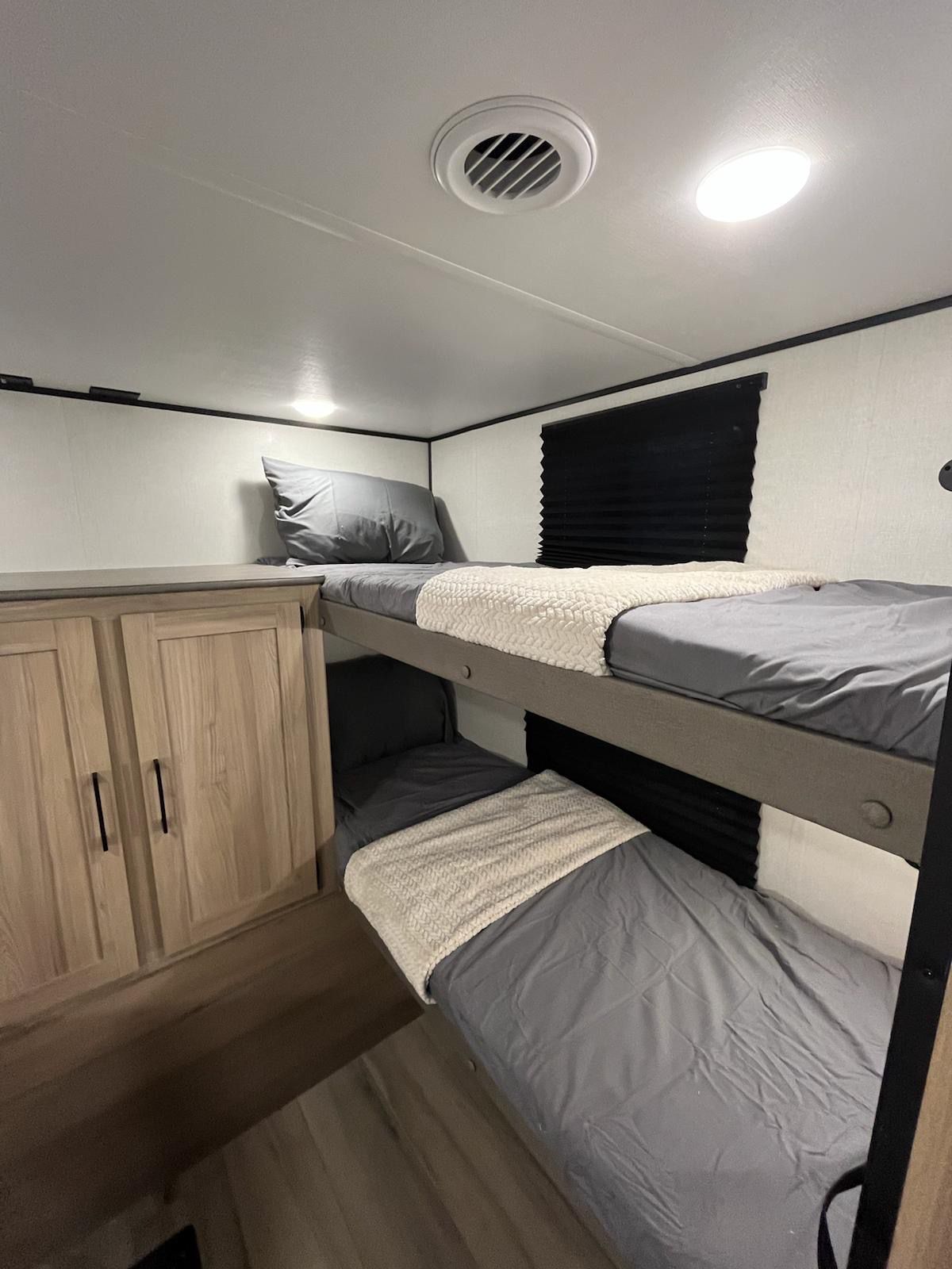Cozy RV rental sleeping area with gray bedding on bunk beds, a white throw, and a wooden storage cabinet.. Dutchmen Coleman 2025