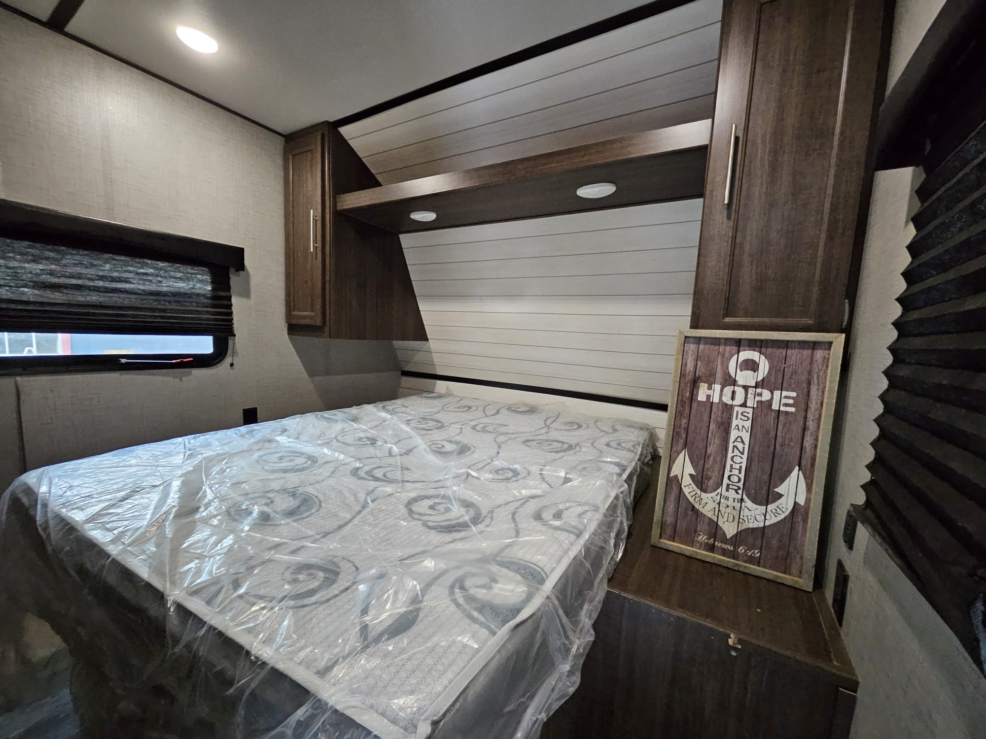 RV rental bedroom with a plastic-covered mattress, built-in storage, and an anchor-themed decorative sign.. Crossroads RV Zinger 2019