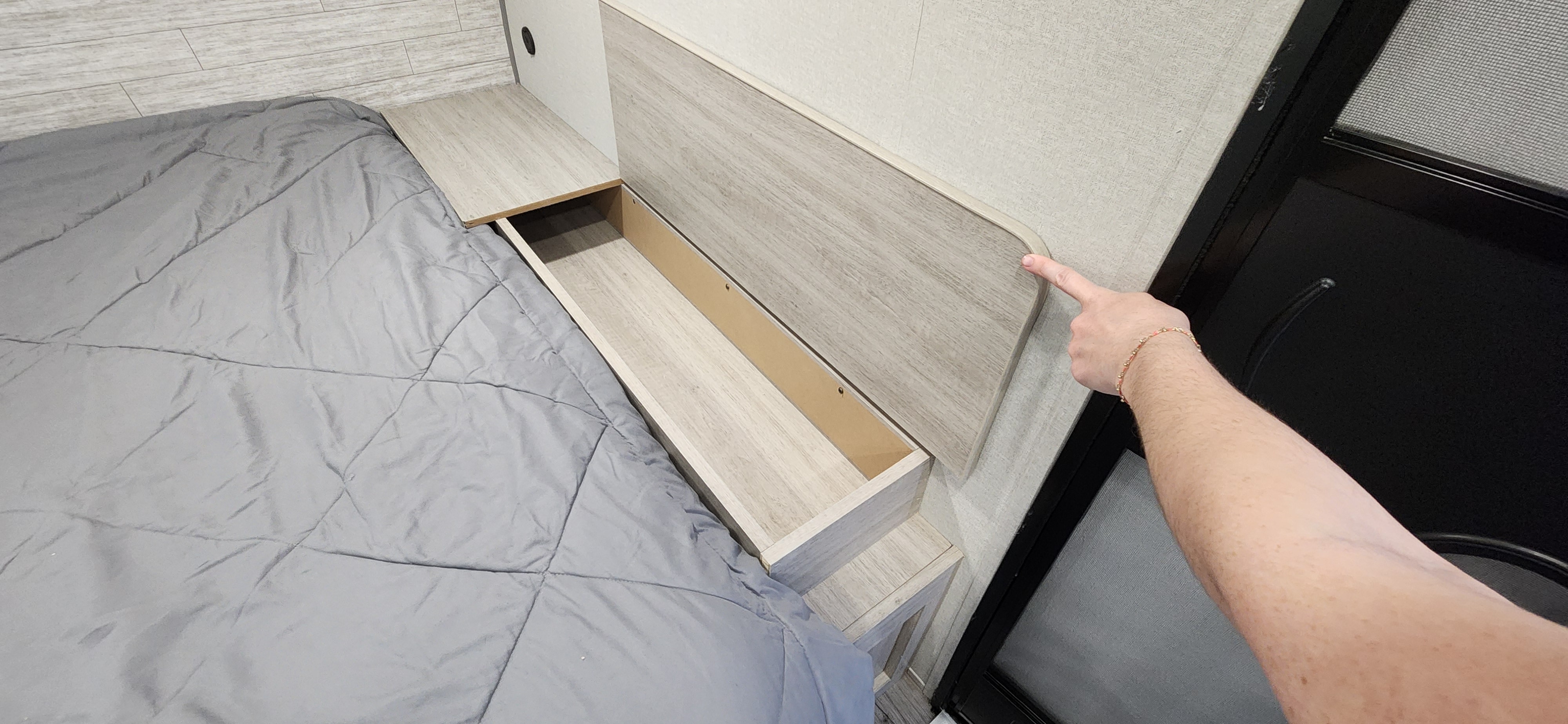 Compact RV rental bedroom features a comfy bed and clever bedside storage. A finger points to the integrated headboard design.. Forest River Catalina Summit Series 2024