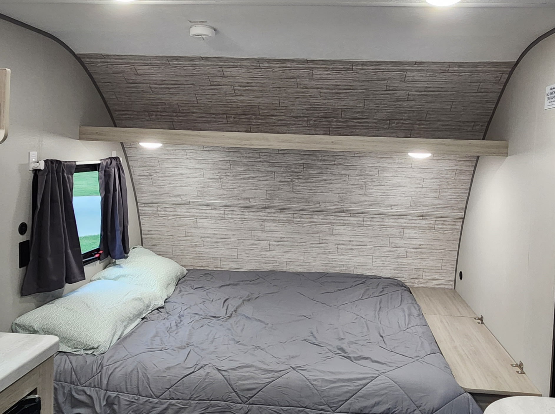 Cozy RV rental bedroom with gray bedding, wood-paneled walls, a built-in shelf, and recessed lighting.. Forest River Catalina Summit Series 2024