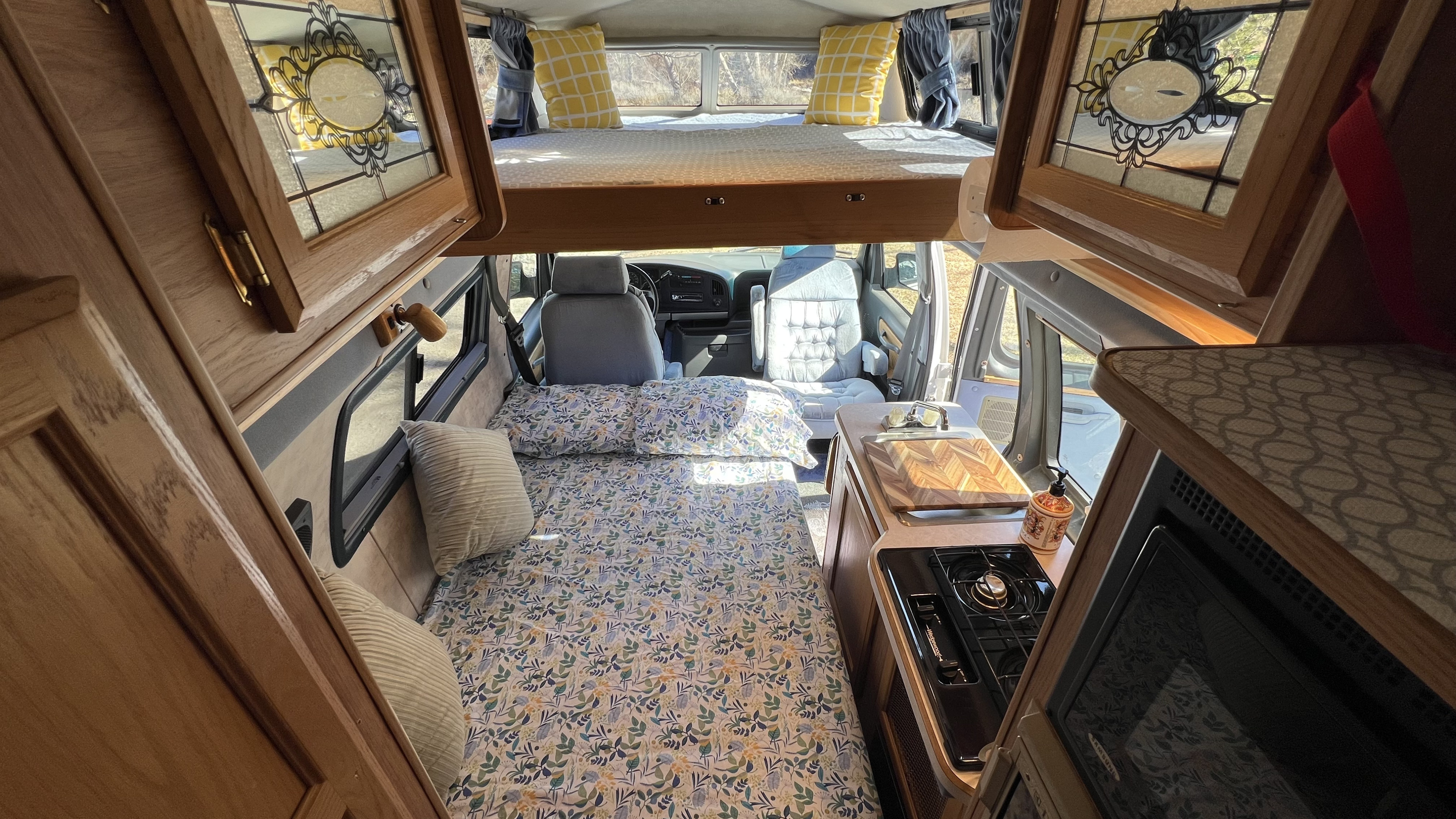This rv rental interior shows a main bed, upper bunk, kitchen area with stove/sink, and the driver's cabin.. Coachmen Van Conversion 1994