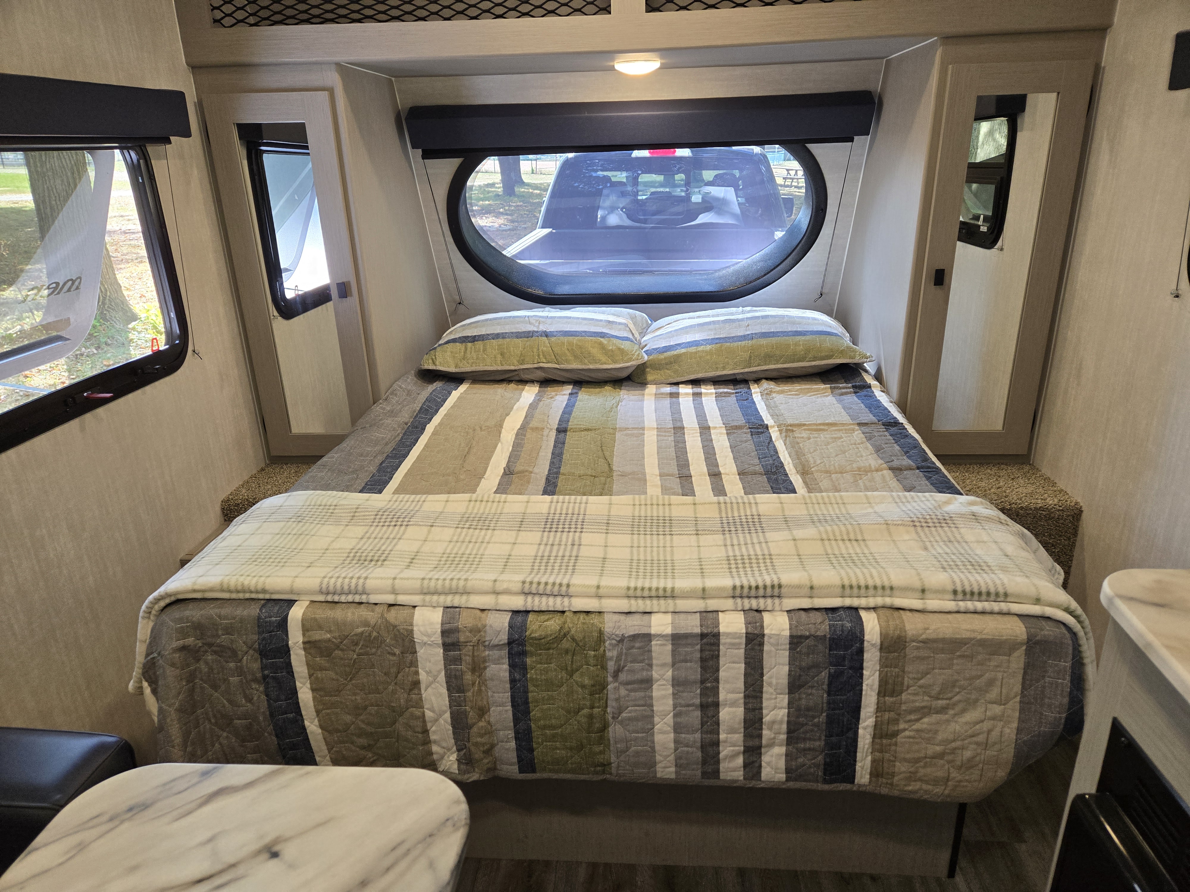 Inside an RV rental, a cozy bedroom features a bed with striped bedding and a unique round window view.. Coachmen Remote 2024