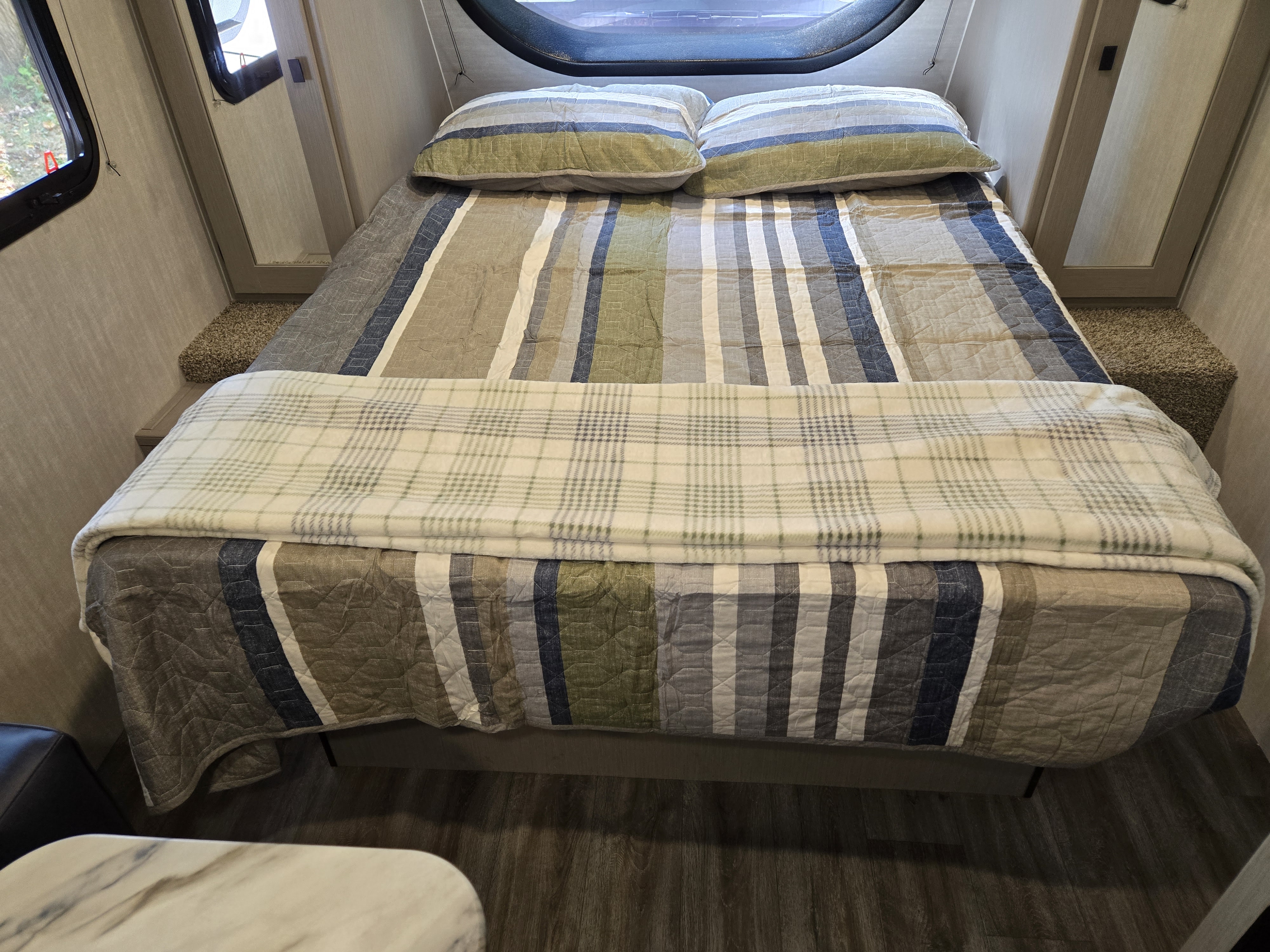 Cozy RV rental bedroom with striped bedding and plaid throw blanket, offering comfortable sleeping quarters.. Coachmen Remote 2024