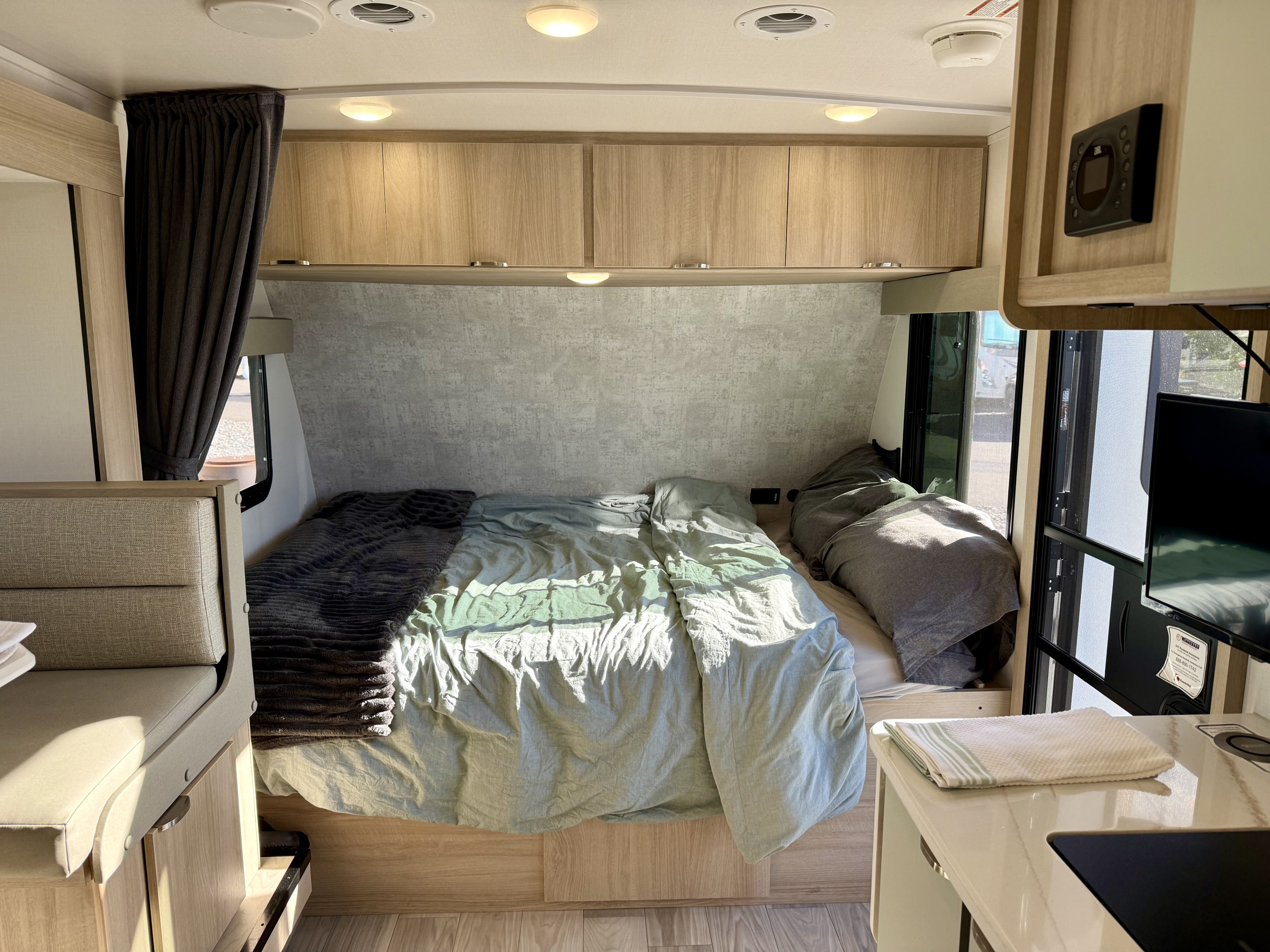 Bright RV rental interior shows a bed, light wood cabinets, and compact kitchen area for comfortable travel.. Winnebago Micro Minnie 2025