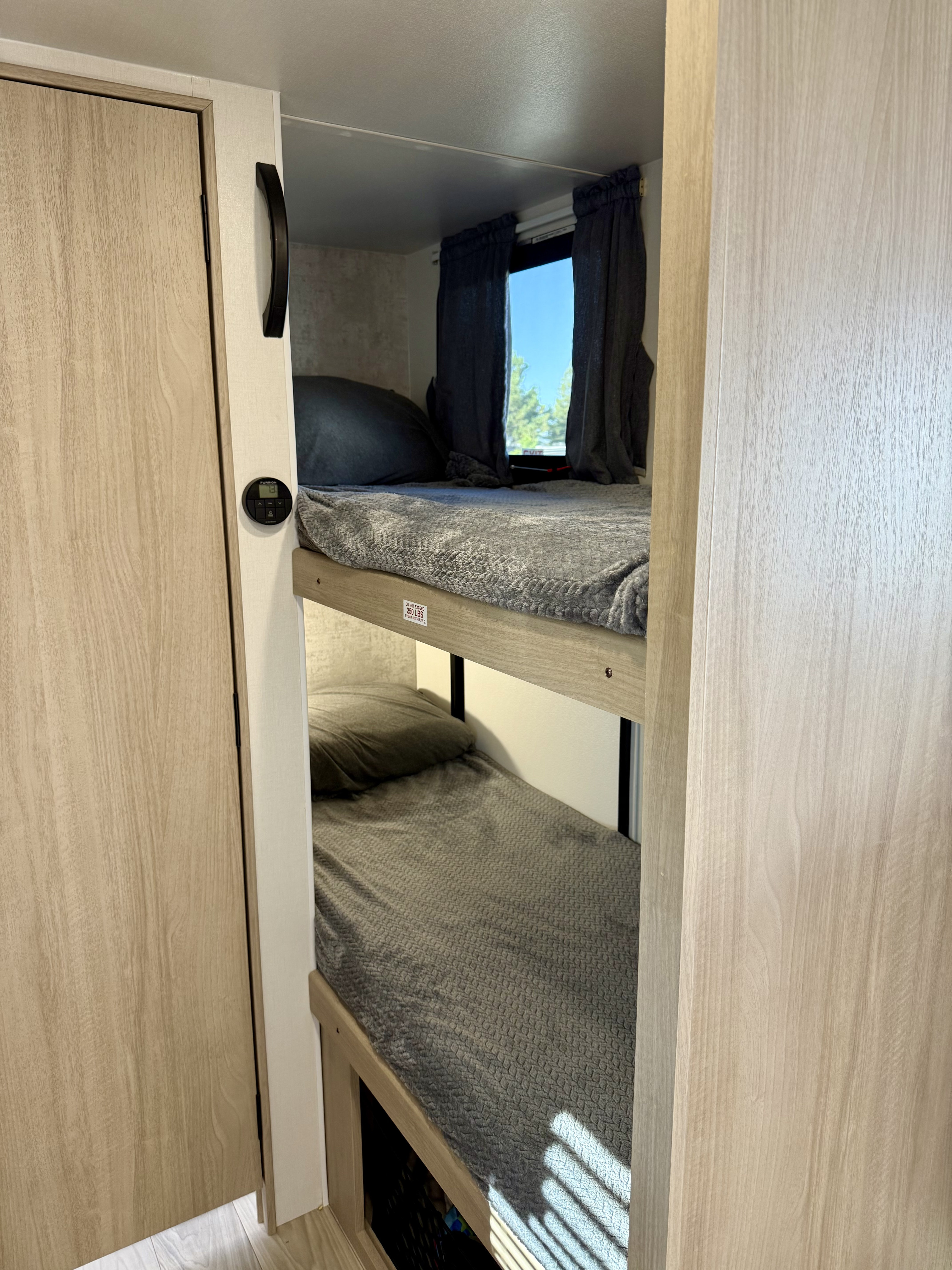 Cozy RV rental bunk beds with gray bedding and a window, ideal for extra sleeping space.. Winnebago Micro Minnie 2025