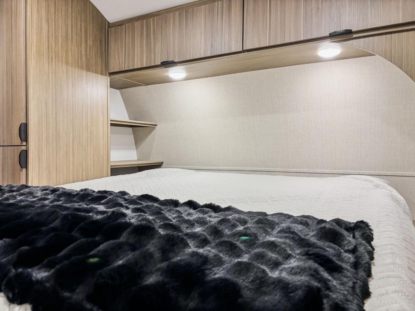 Inside an RV rental: a tidy bedroom with wood cabinets, built-in shelves, and a cozy bed with a dark blanket.. Forest River Salem 2025
