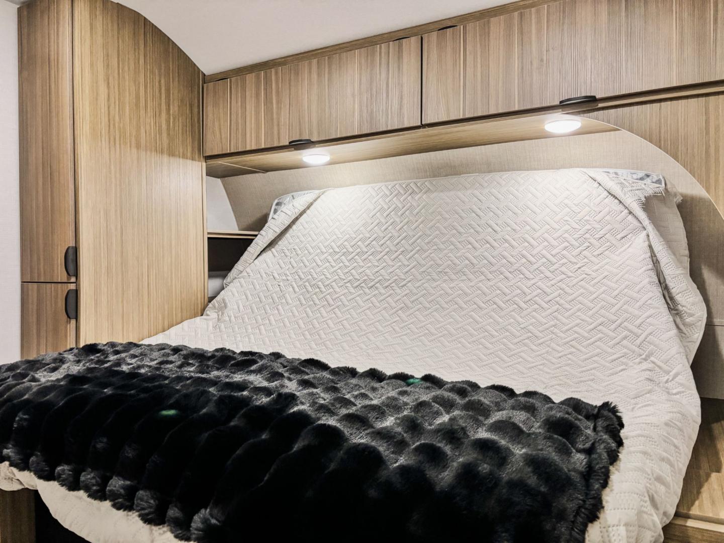 Cozy RV rental bedroom featuring built-in storage, a bed with a white patterned comforter, and black fuzzy throw blanket.. Forest River Salem 2025