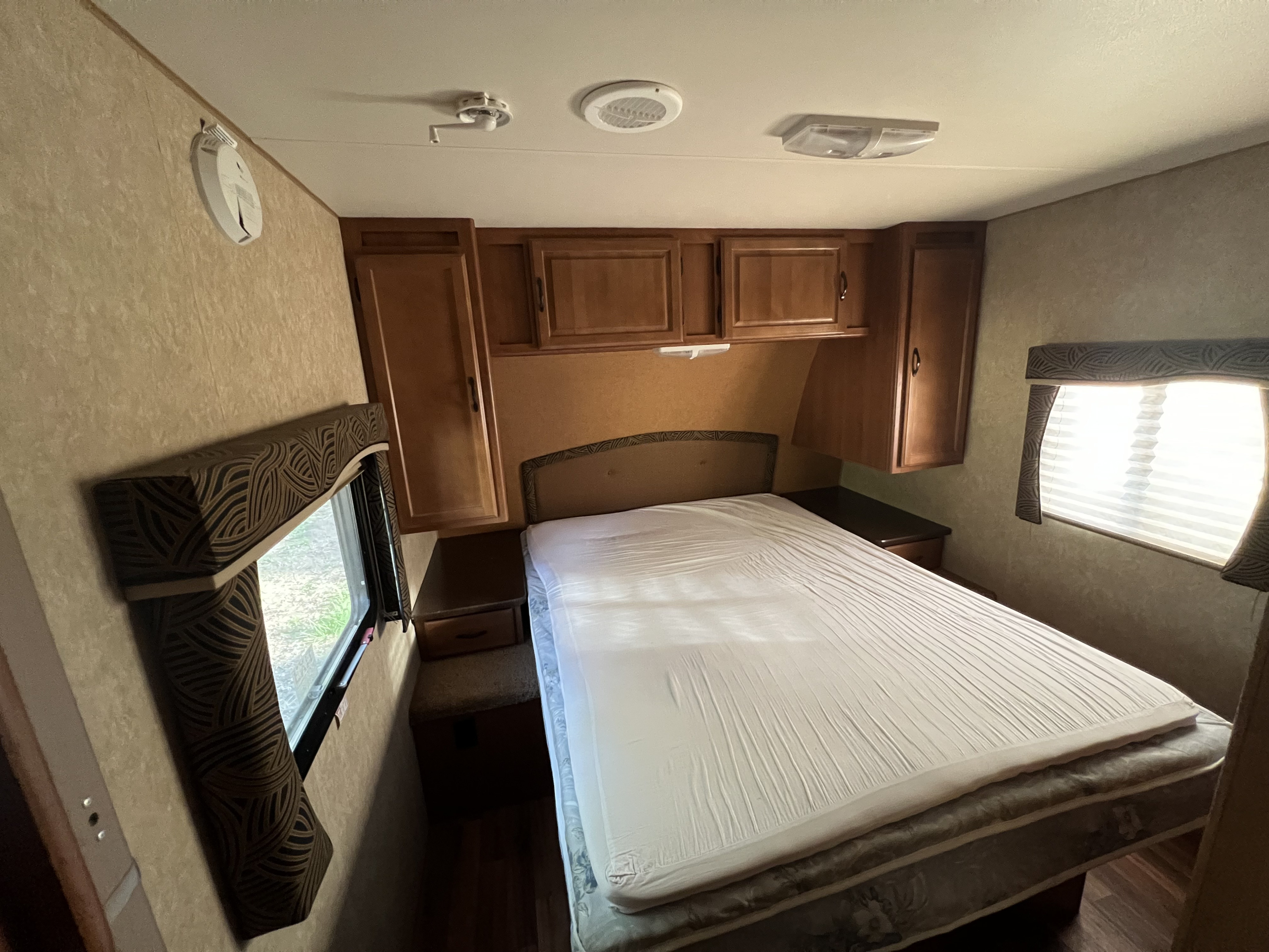 RV rental bedroom interior with a large bed, wood overhead cabinets, and two bright windows. Perfect for your next trip.. Komfort Trailblazer 2011