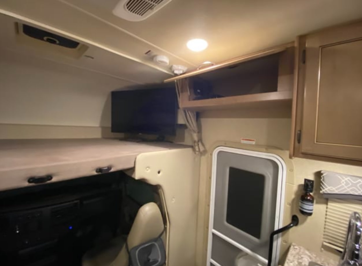 RV rental interior view: shows an overhead bunk, TV, driver's area, door, and kitchen with cabinets.. Thor Chateau 2019