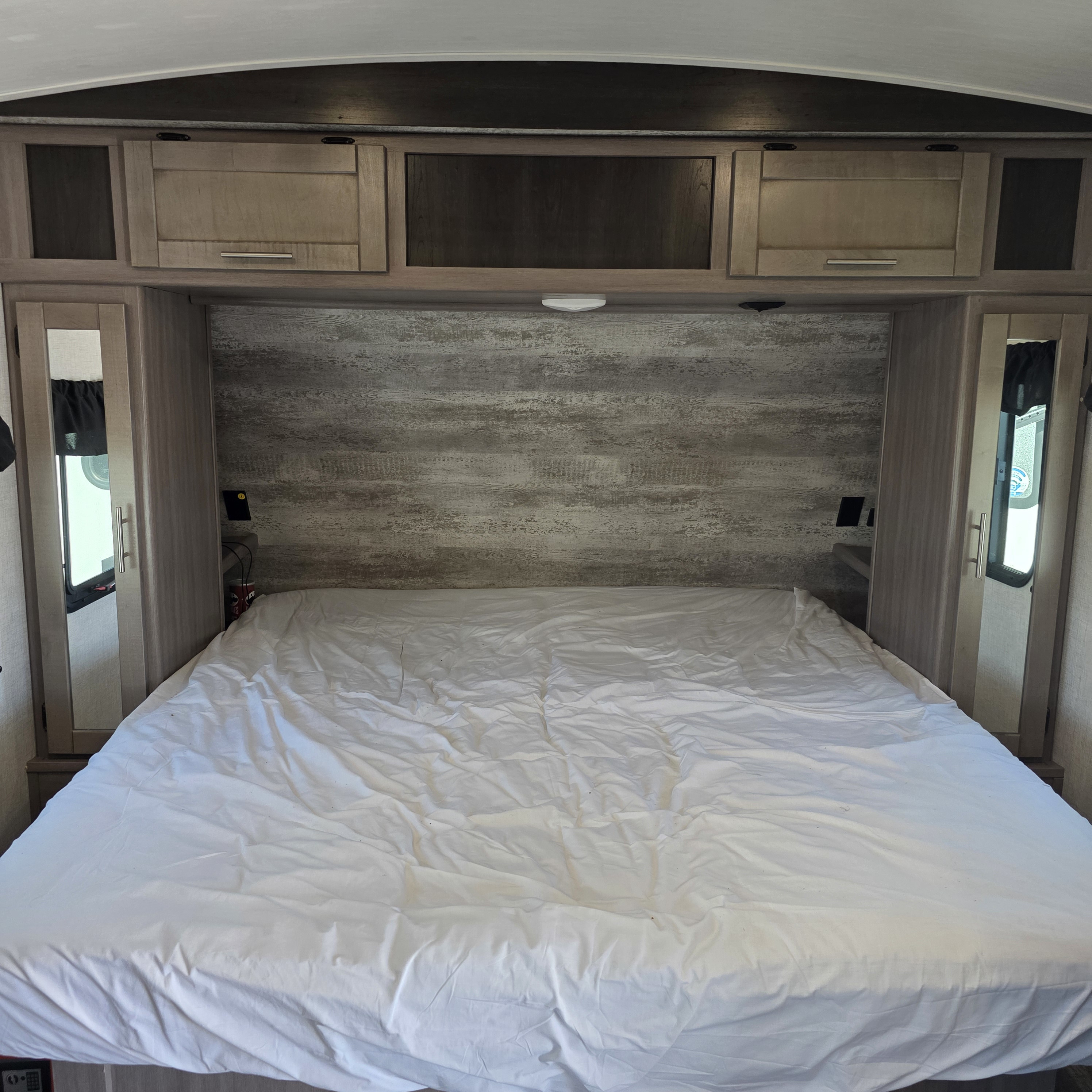 An RV rental bedroom featuring a full bed with white sheets, built-in storage cabinets, and warm wood paneling.. Crossroads RV Sunset Trail Super Lite 2022