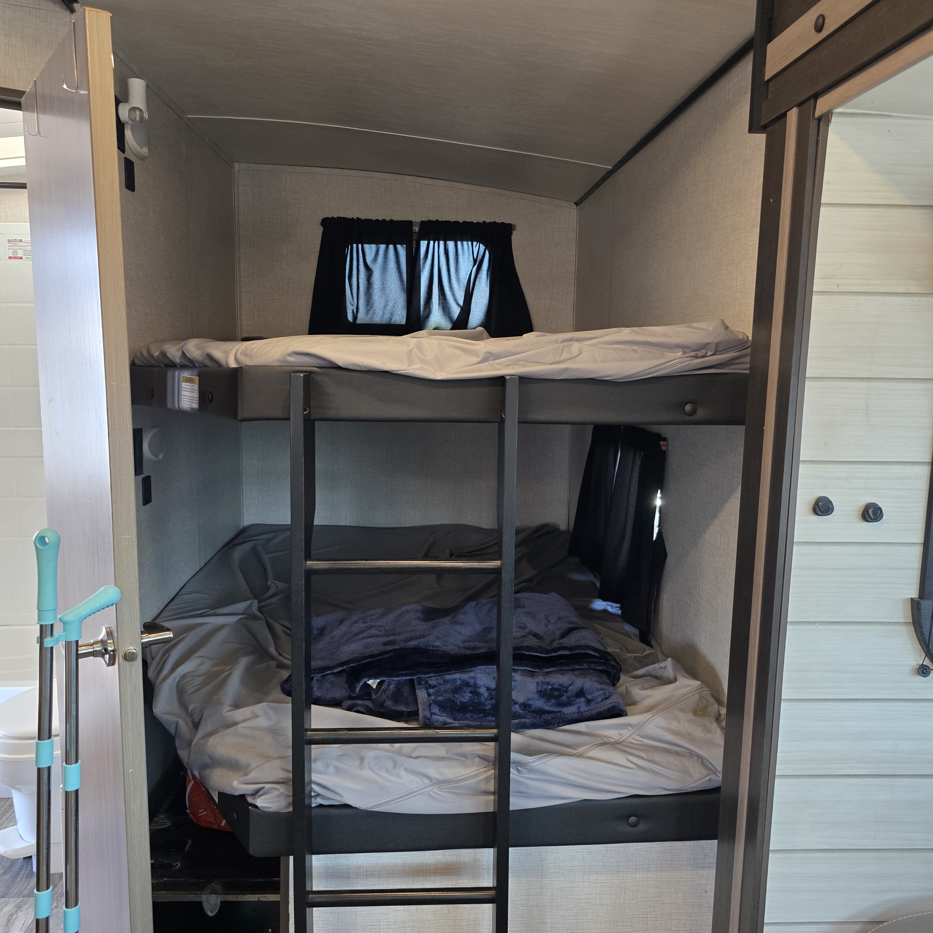 RV rental interior features neat grey bunk beds with a black ladder, and a window. A compact, functional sleeping space.. Crossroads RV Sunset Trail Super Lite 2022