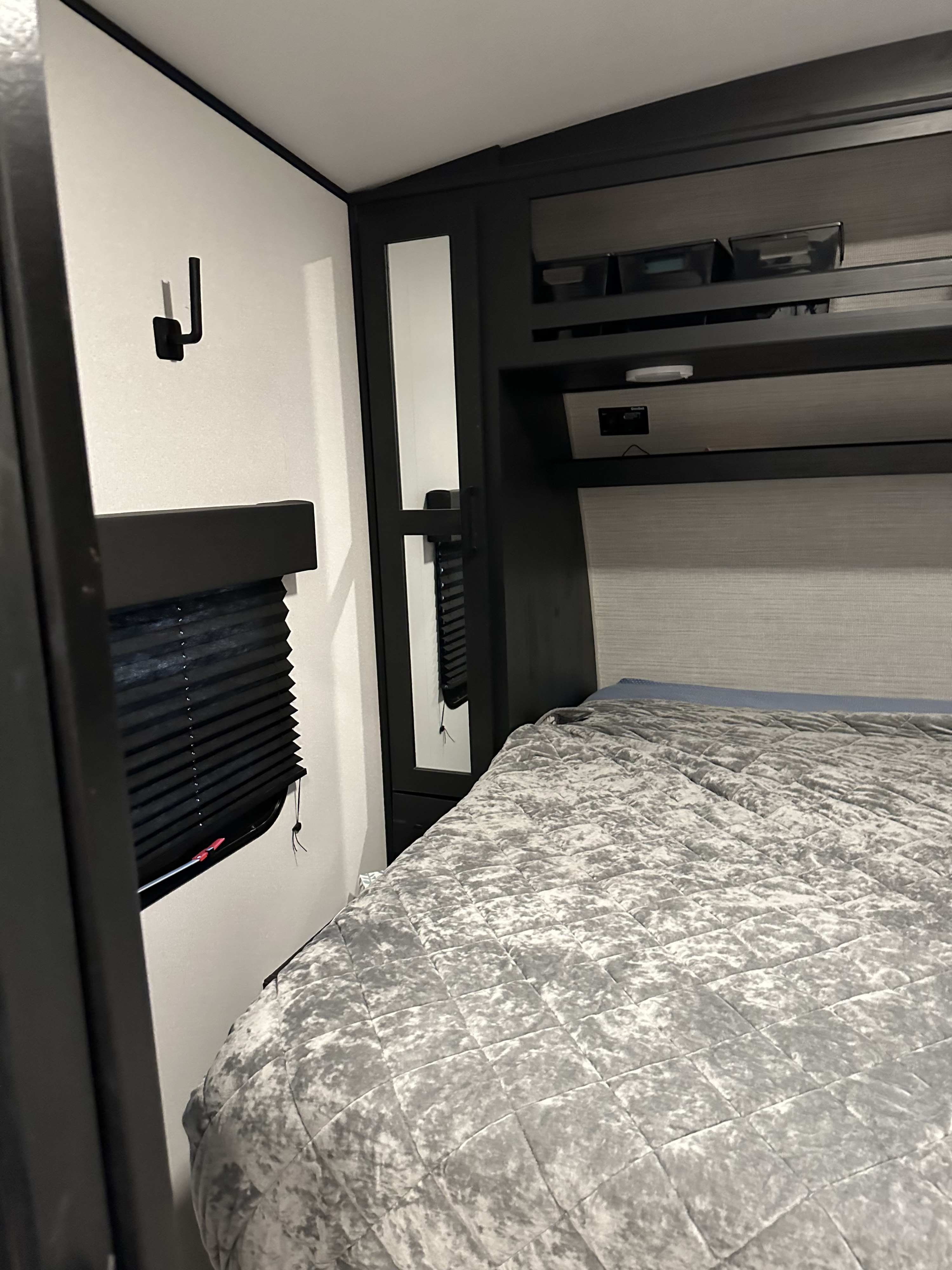 Modern RV rental bedroom featuring a comfy gray bed, ample overhead storage, and a private window with a shade.. Heartland Fuel 287 2022