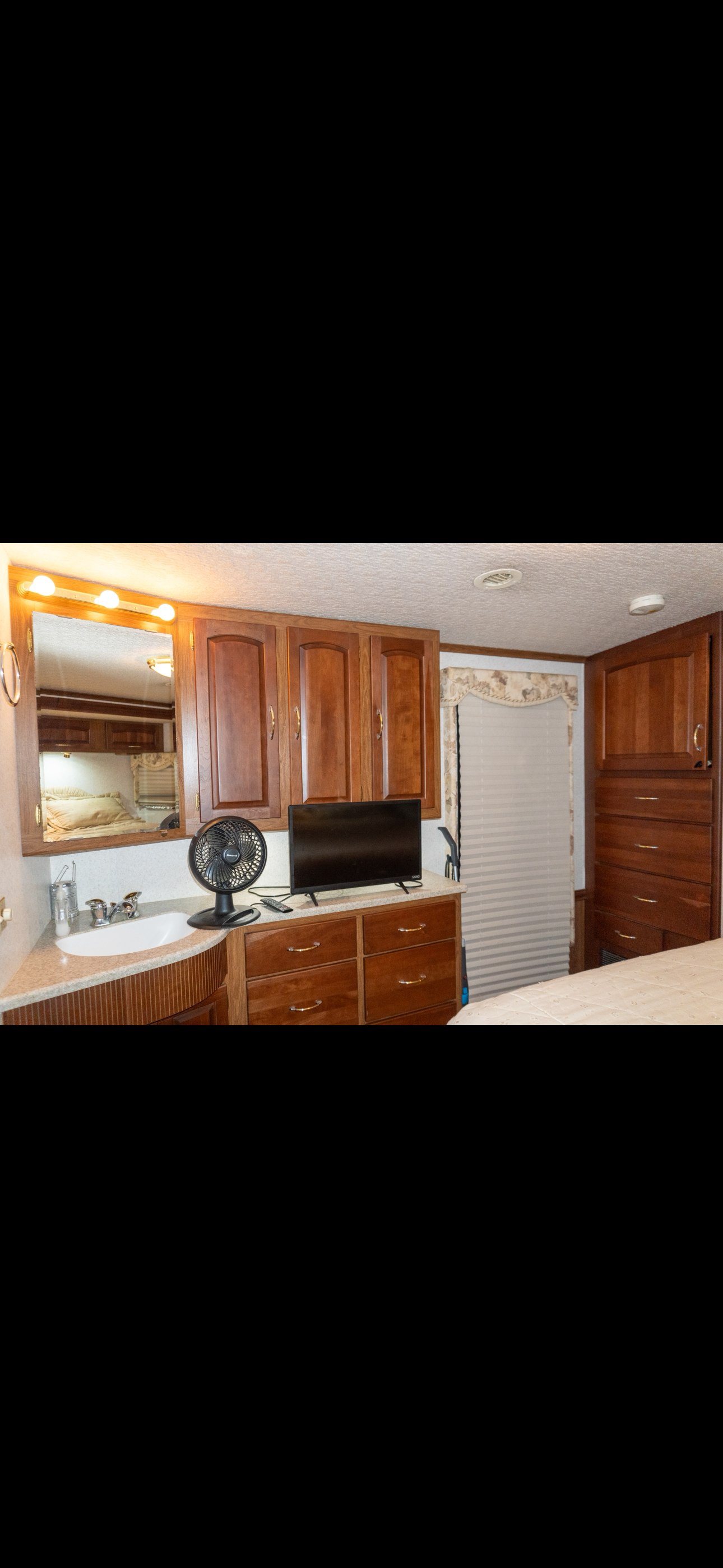 This RV rental offers a well-appointed bedroom with a vanity sink, mirror, wooden cabinets, dresser, and TV for a comfortable stay.. Itasca Horizon 2002