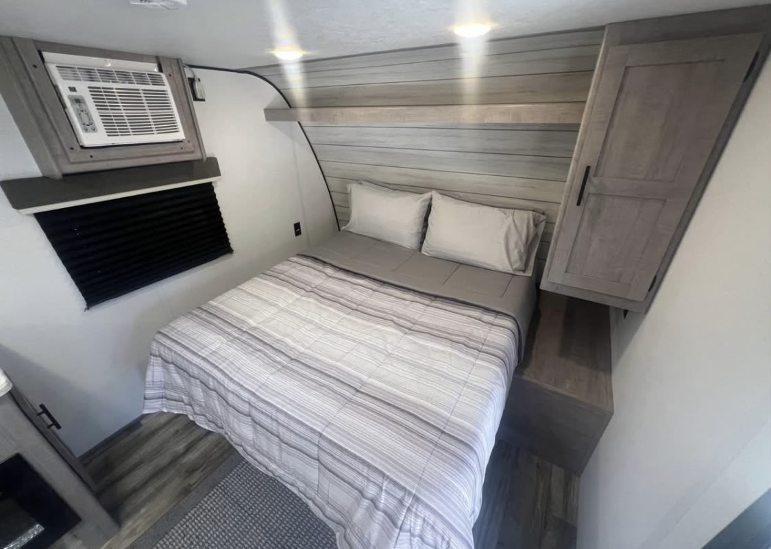 RV rental bedroom showcasing a comfortable bed, overhead AC unit, wood paneled walls, and convenient storage.. Dutchmen LT 17R 2024